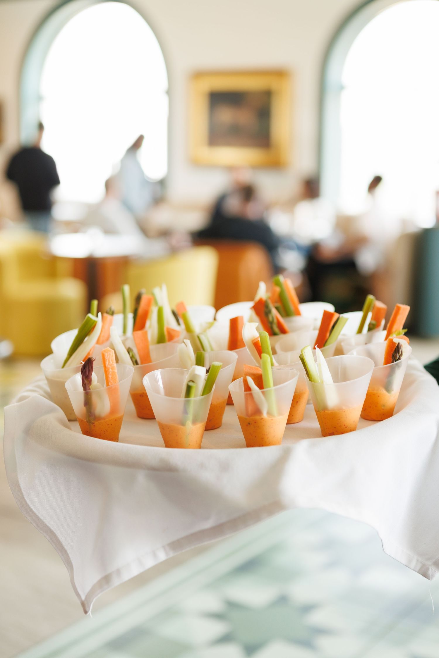 Elegant appetizer cups with fresh vegetables and dipping sauce served on a white linen tray at a catered event.
