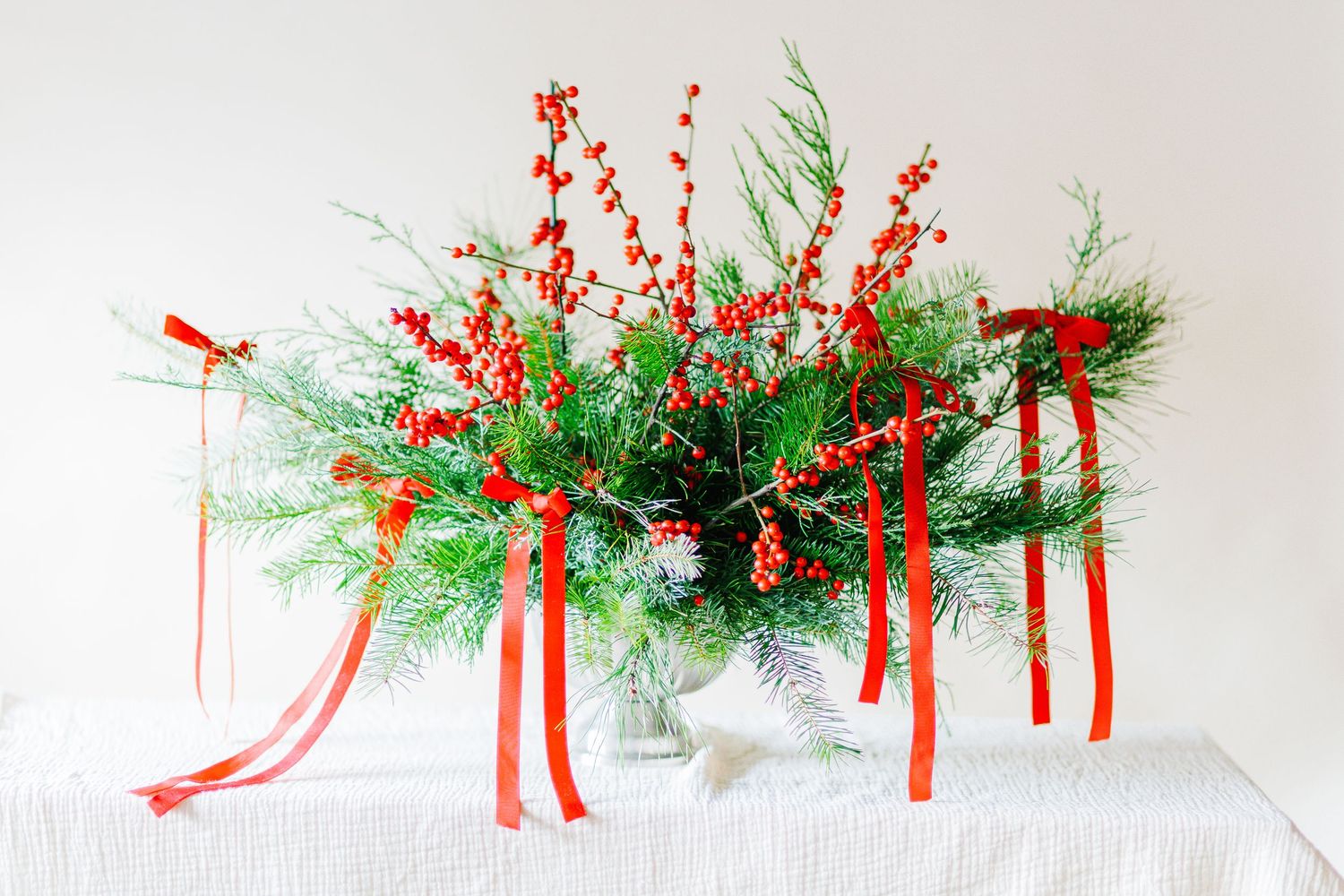 Evergreen garland with red ribbons decorates a white surface for holiday decor.