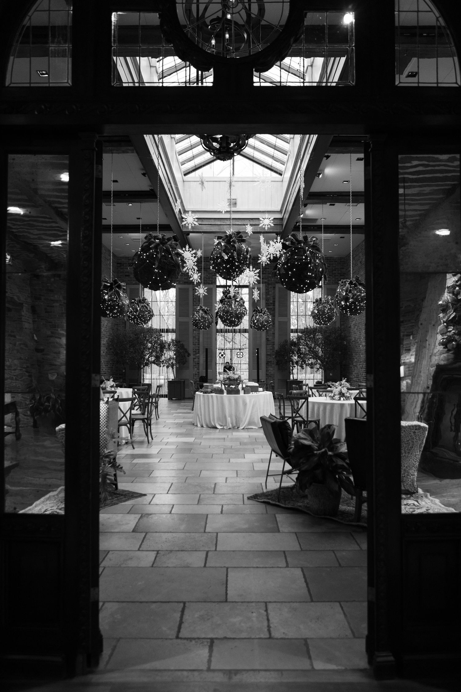 Black and white view of elegant reception venue with skylight and hanging floral arrangements.