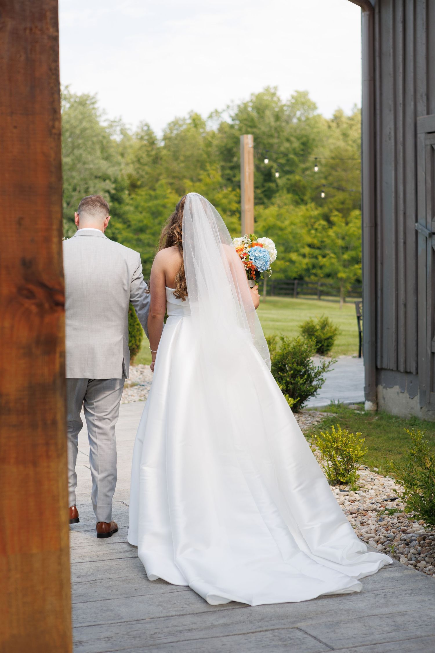 Bride and groom walking hand in hand outdoors, bride wearing white gown with veil holding colorful bouquet.