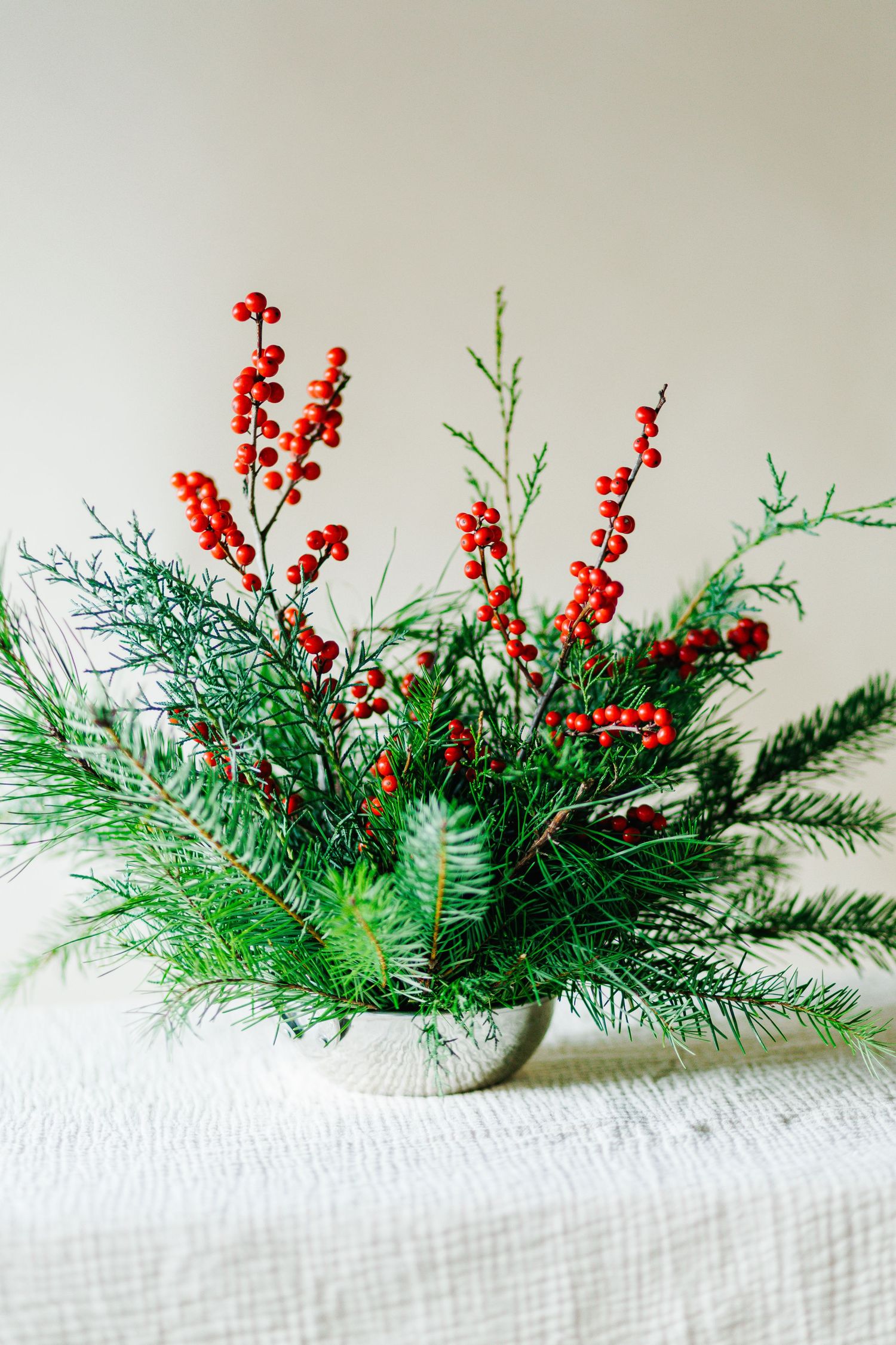 Fresh pine branches arranged with red winter berries on white linen.