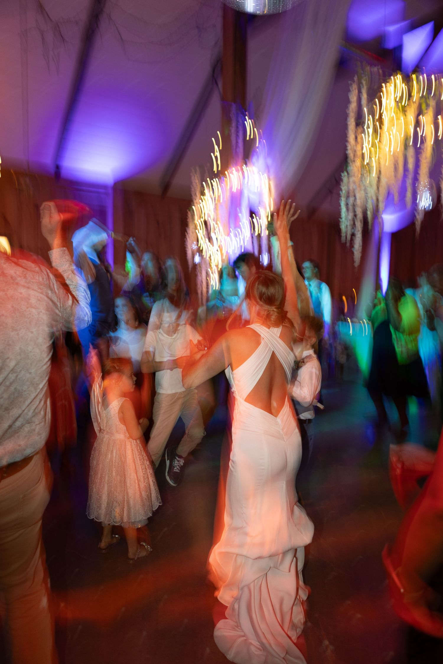 Motion-blurred dancers at a wedding reception under purple and blue lighting.