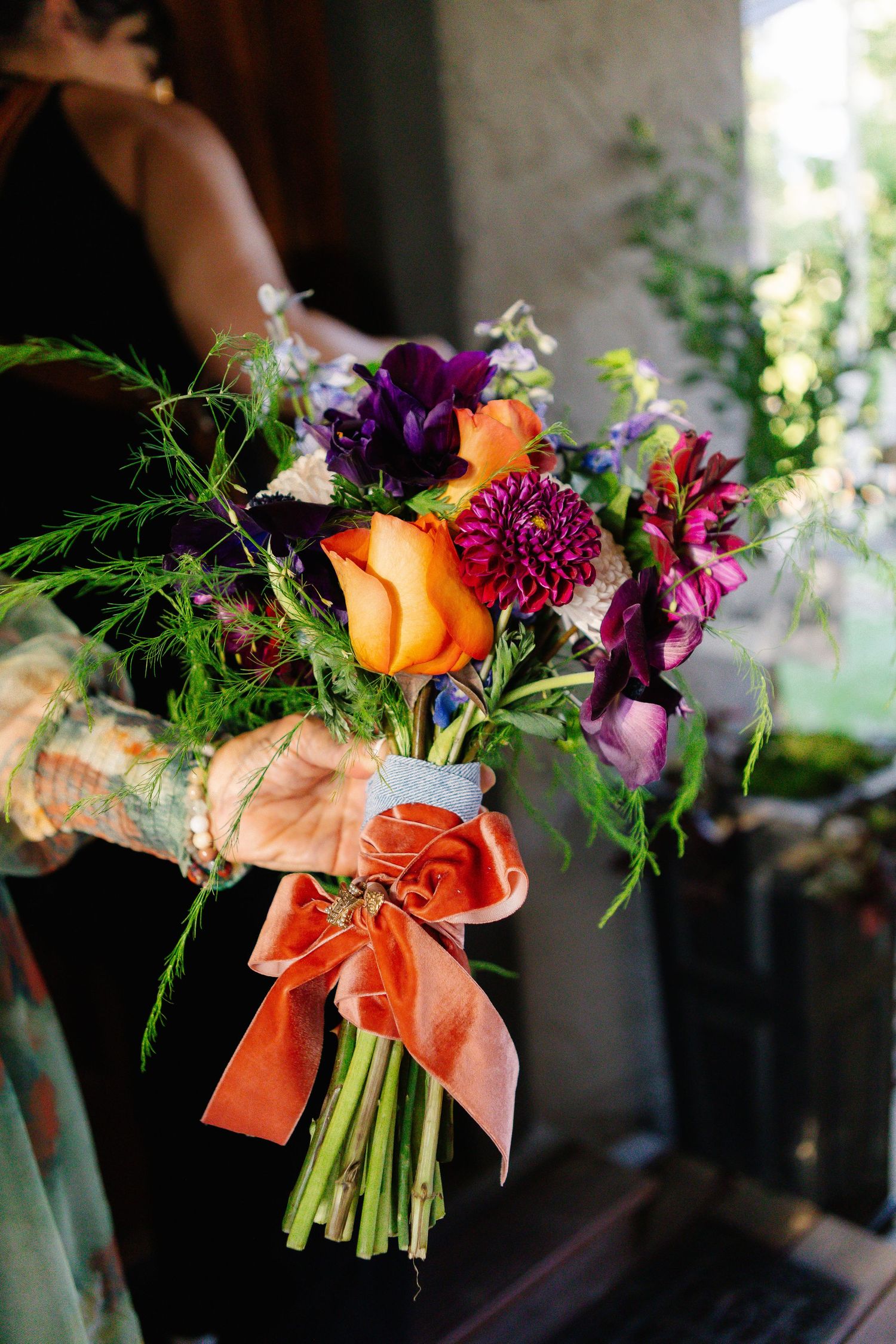 Vibrant wedding bouquet with orange roses and purple flowers tied with coral ribbon.