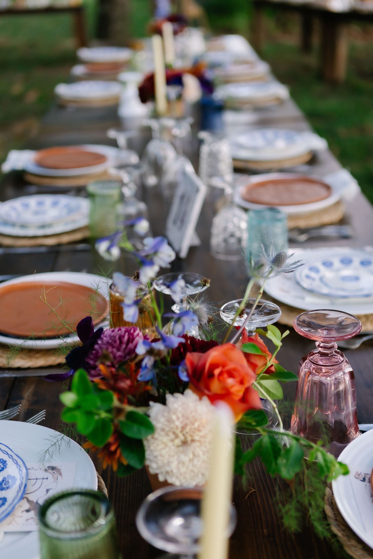 Elegant table setting with vintage plates, crystal glasses and colorful floral arrangements for a garden wedding.