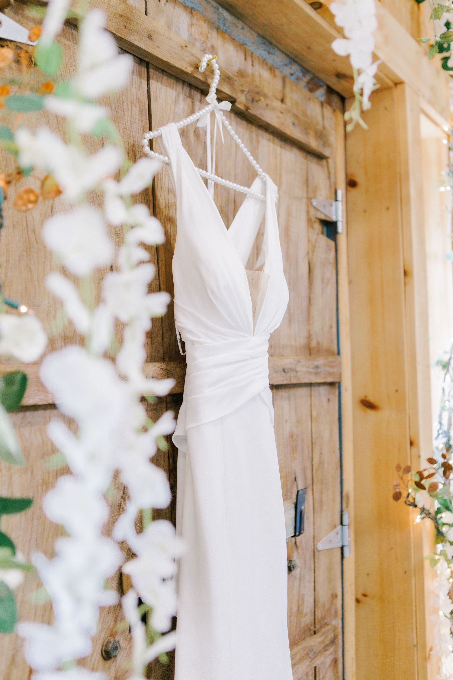 Elegant white wedding dress hanging on rustic wooden door with delicate draping.