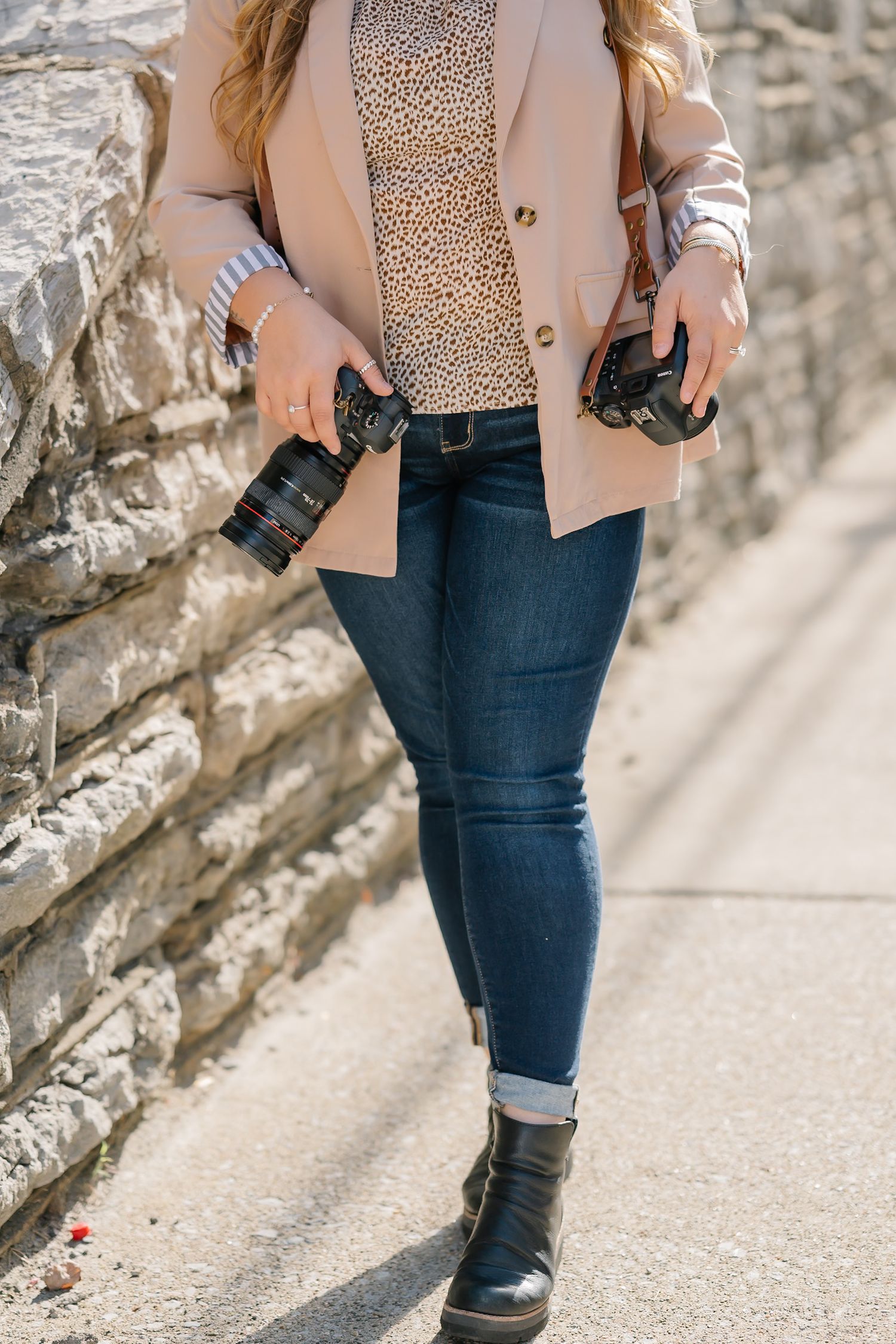 Fashion-forward photographer showcasing camera gear while walking in urban setting.
