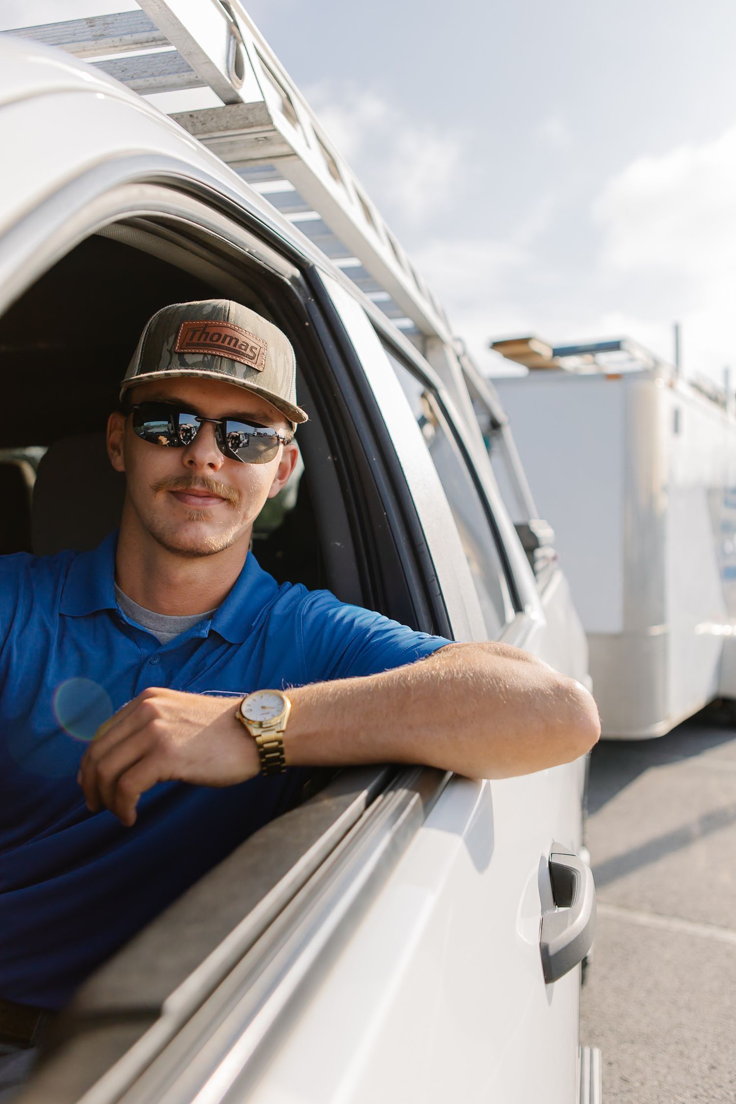 Person in blue shirt and baseball cap smiling while sitting in vehicle cockpit.