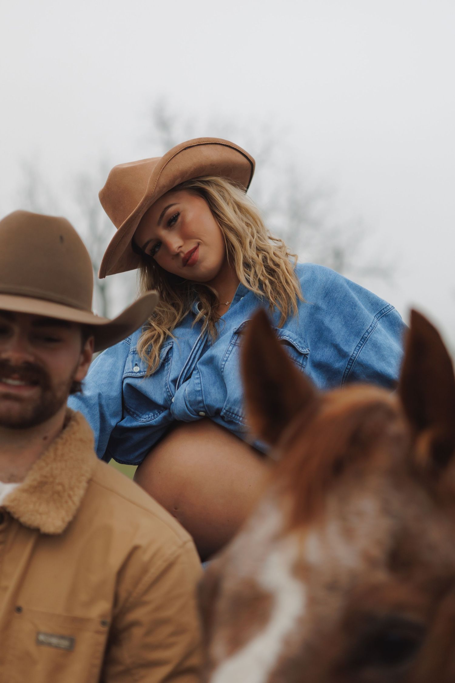 Couple in western attire pose together on a cloudy autumn day.
