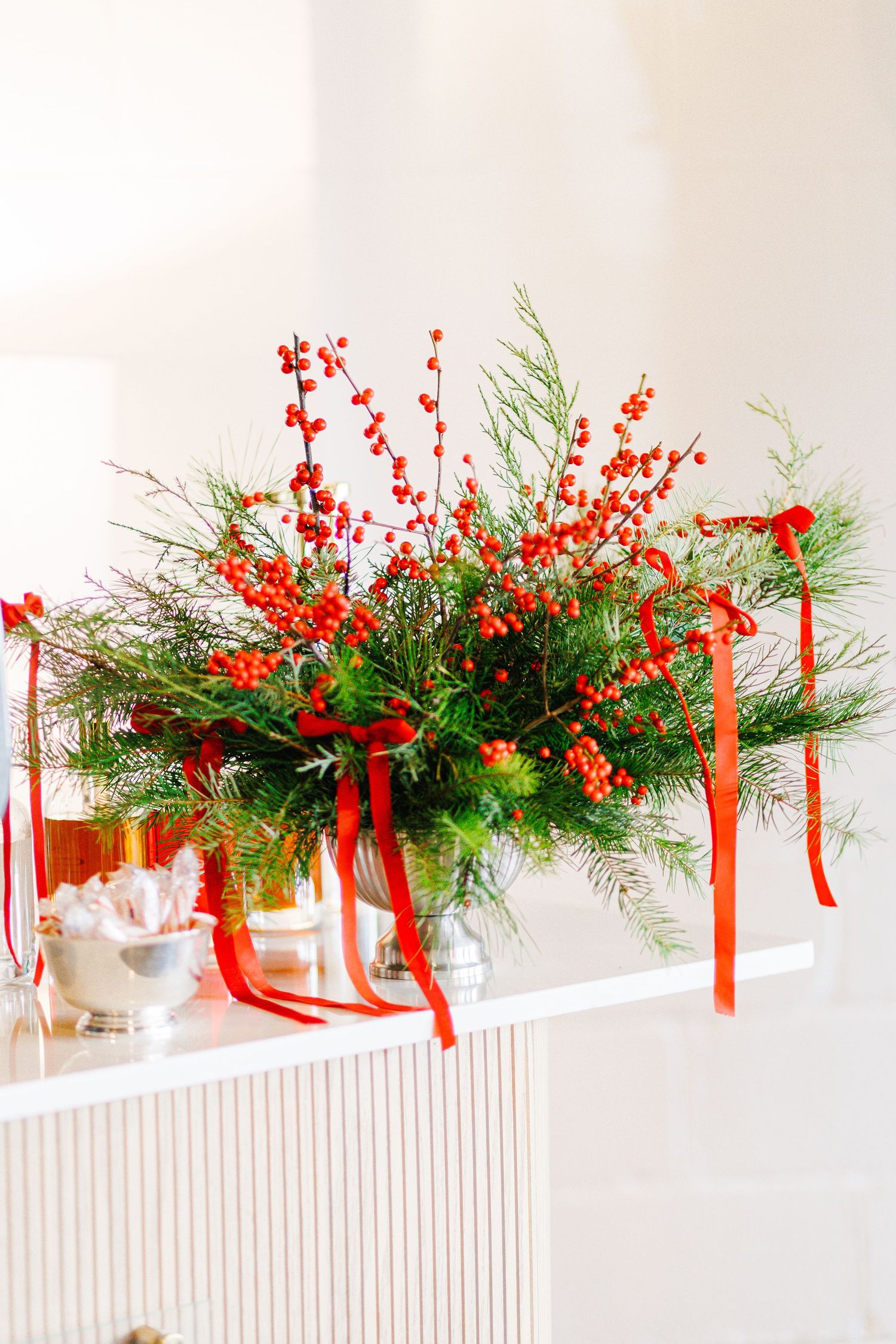 Festive holiday decorations featuring red berries and evergreen branches with ribbons on white shelf.