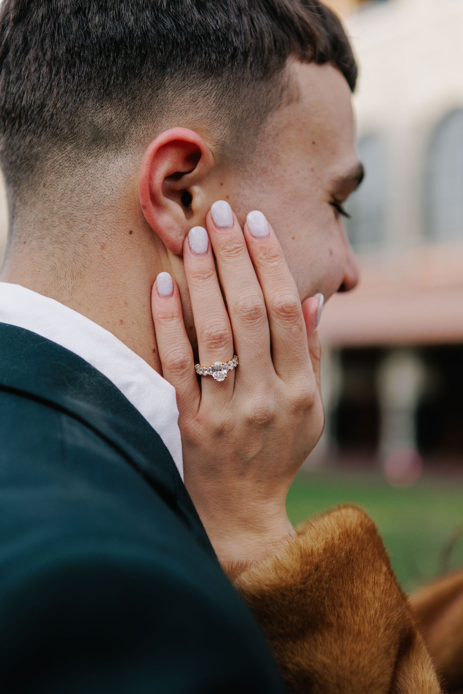 Close-up of hand with engagement ring against formal attire.