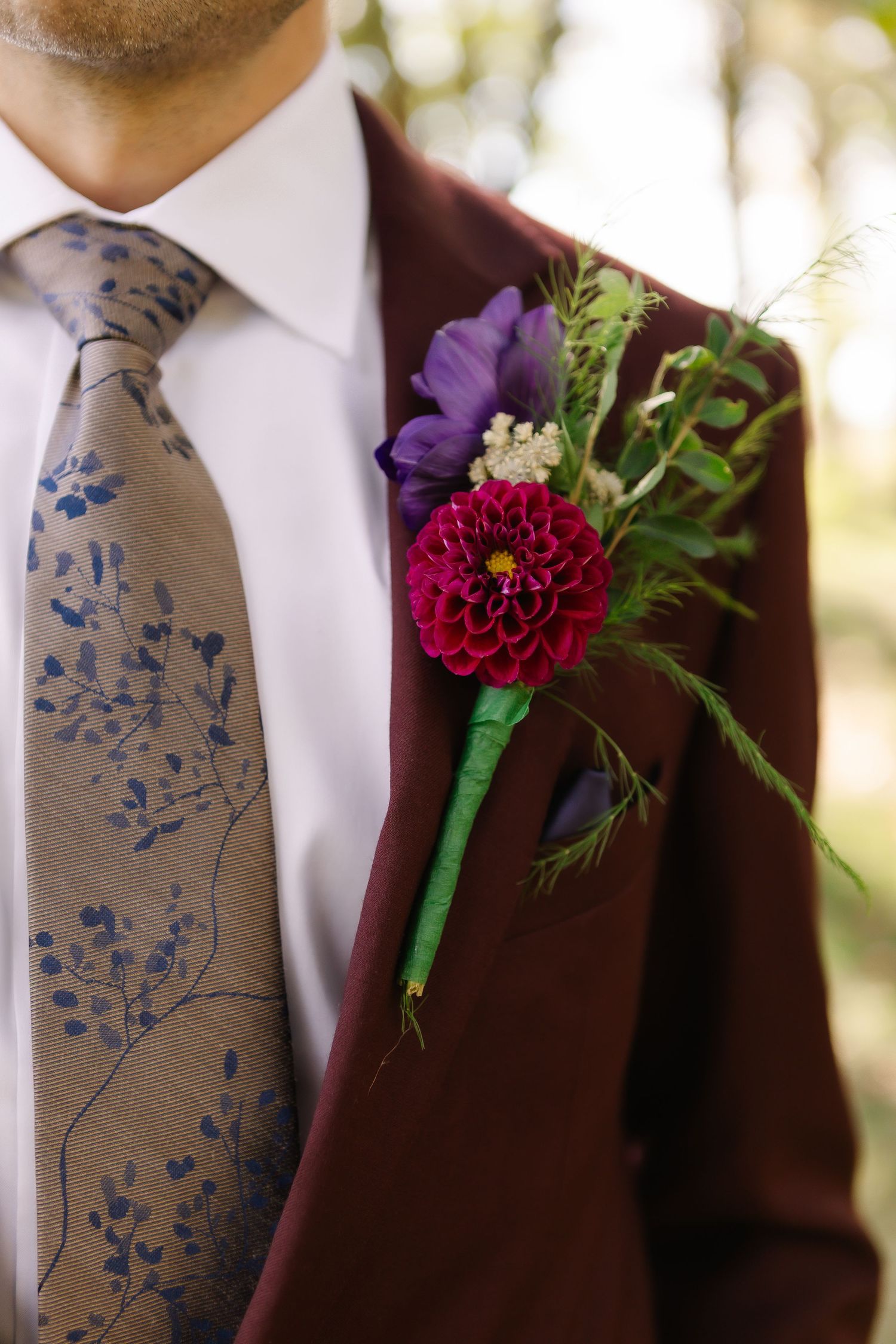 Close-up details of burgundy suit jackets with floral boutonnieres featuring purple and red flowers with green accents.