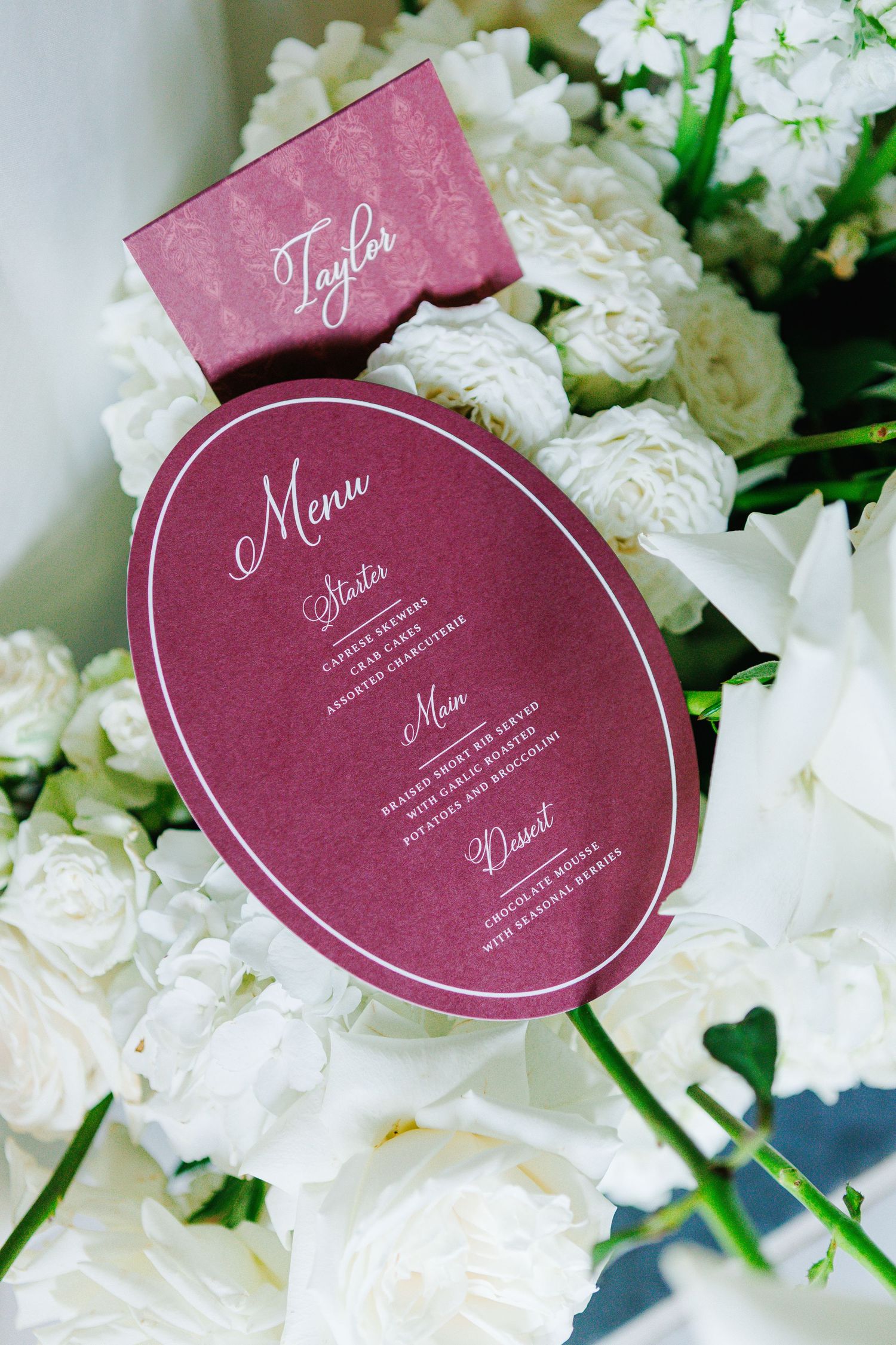 Burgundy circular wedding menu cards nestled among white floral arrangements.