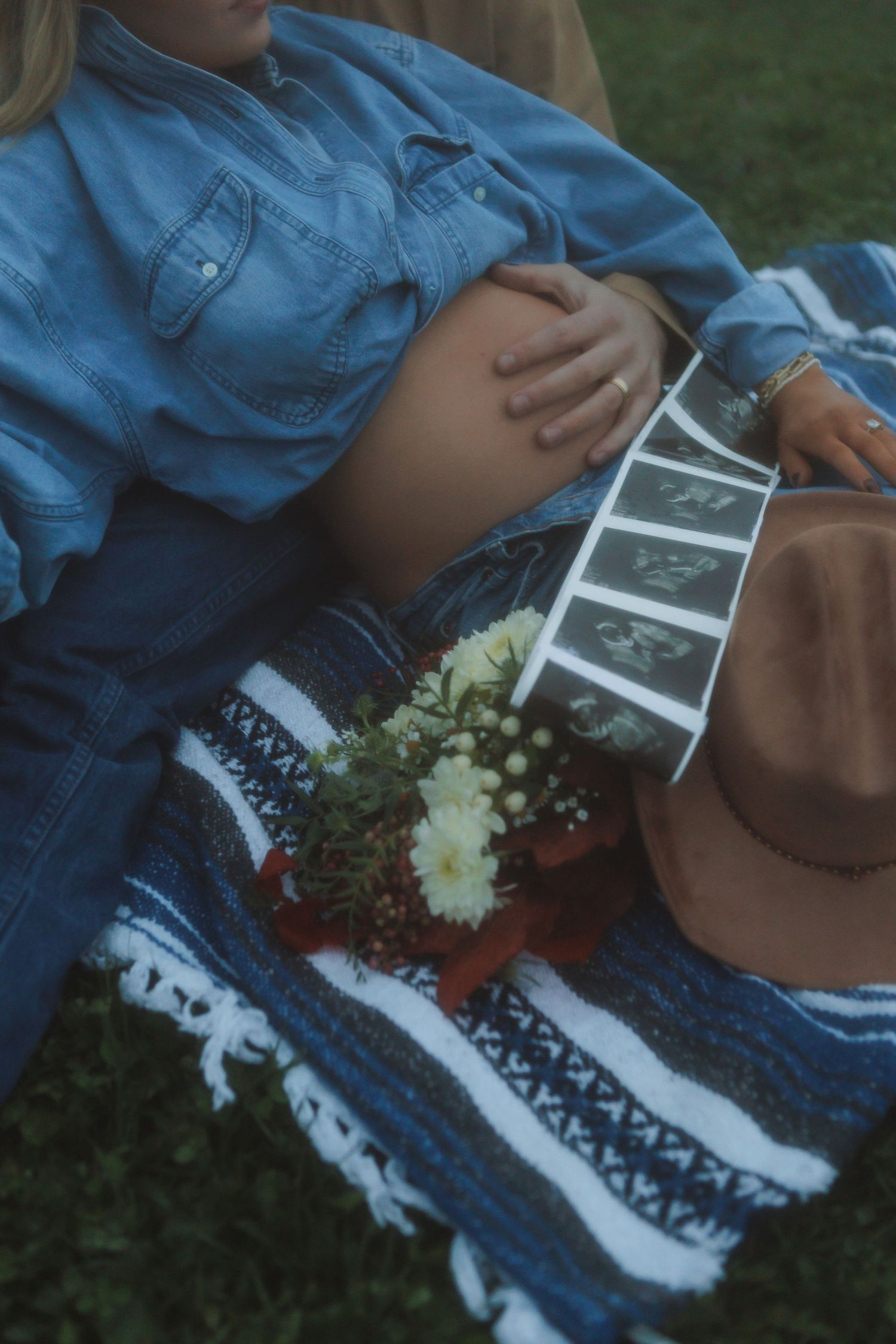 Ultrasound photos and flowers lay on patterned blanket in outdoor setting.
