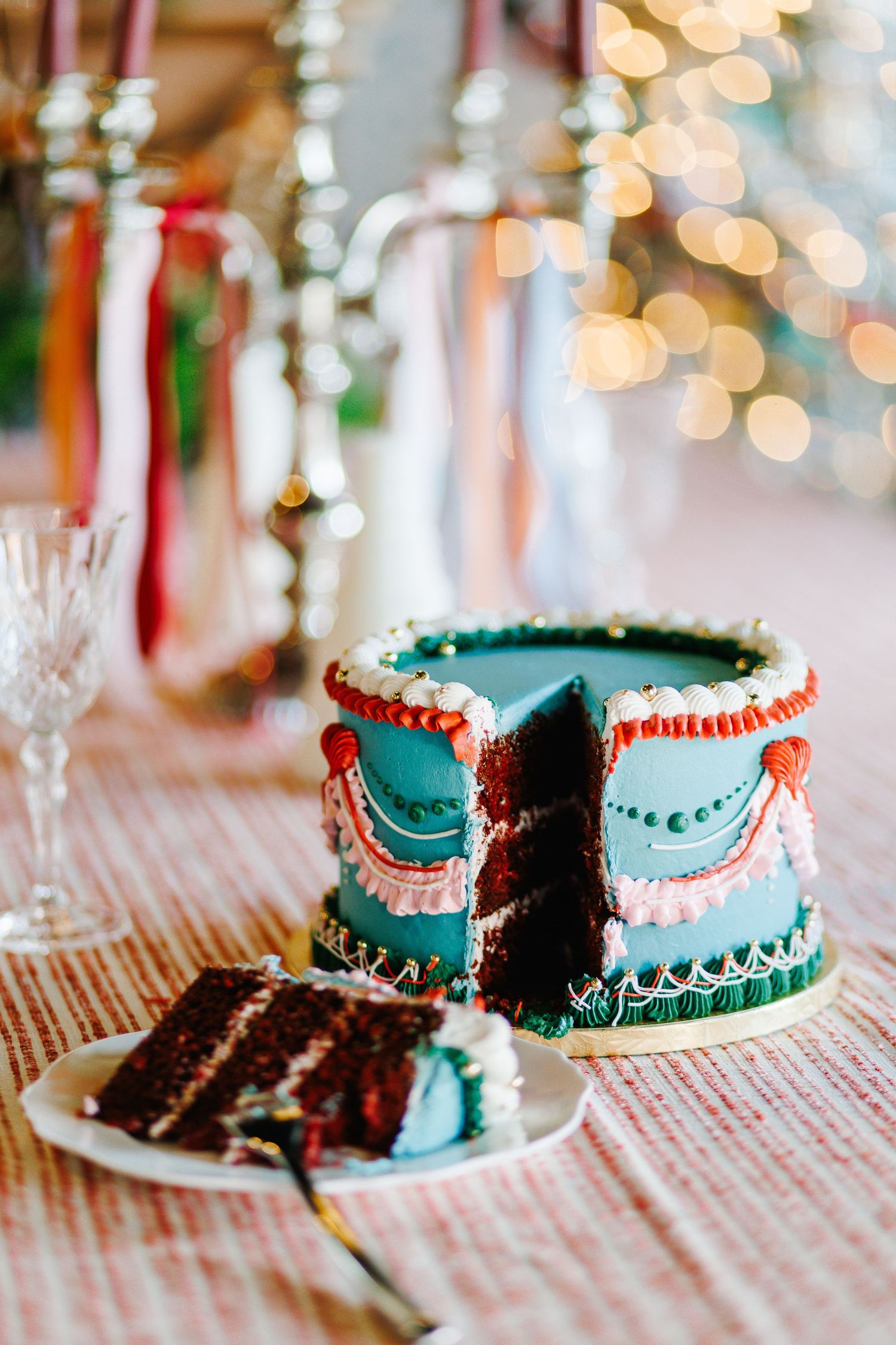 Turquoise and red layered cake with decorative icing details on a striped tablecloth.