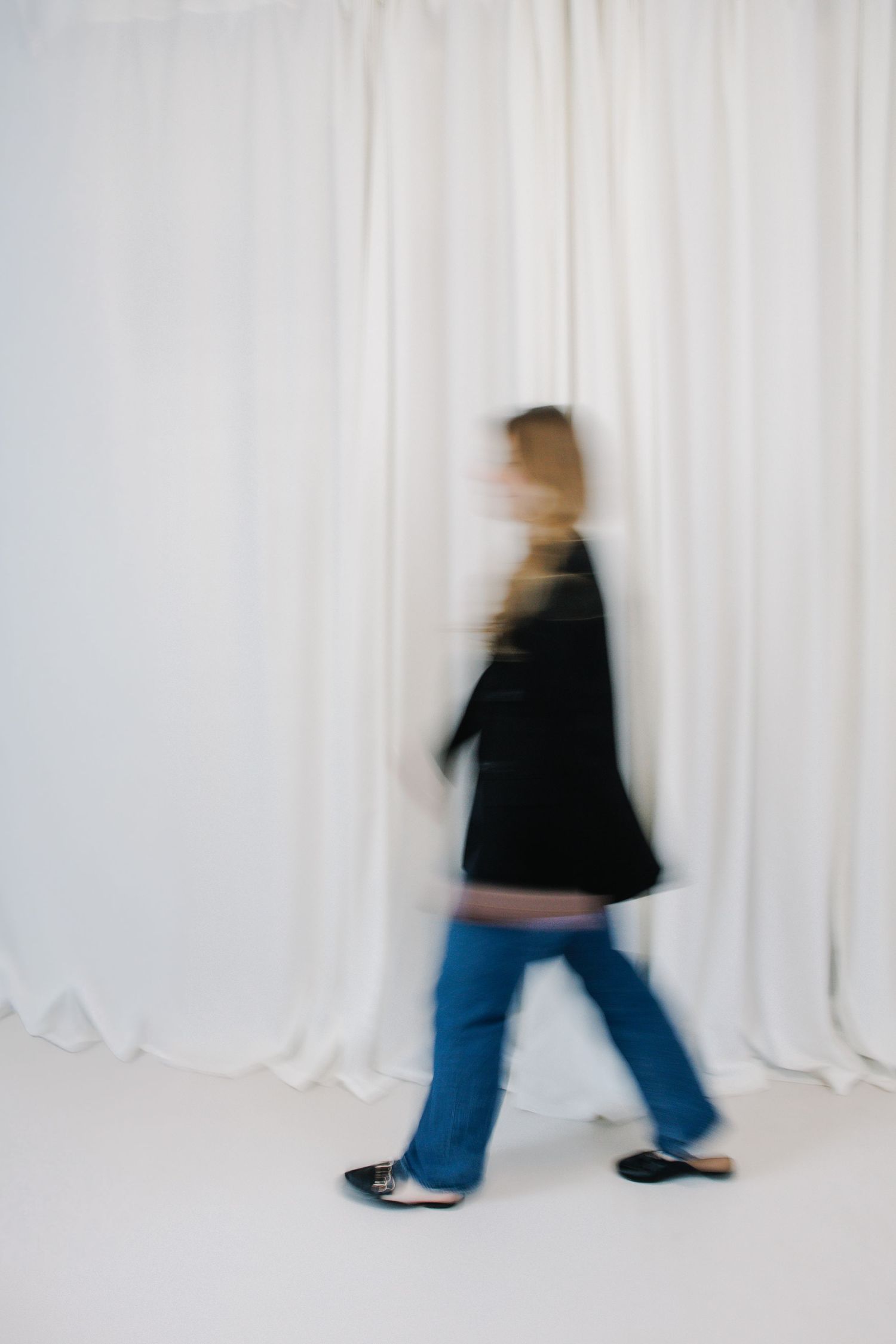 Motion blur sequence of person walking past white curtain background.