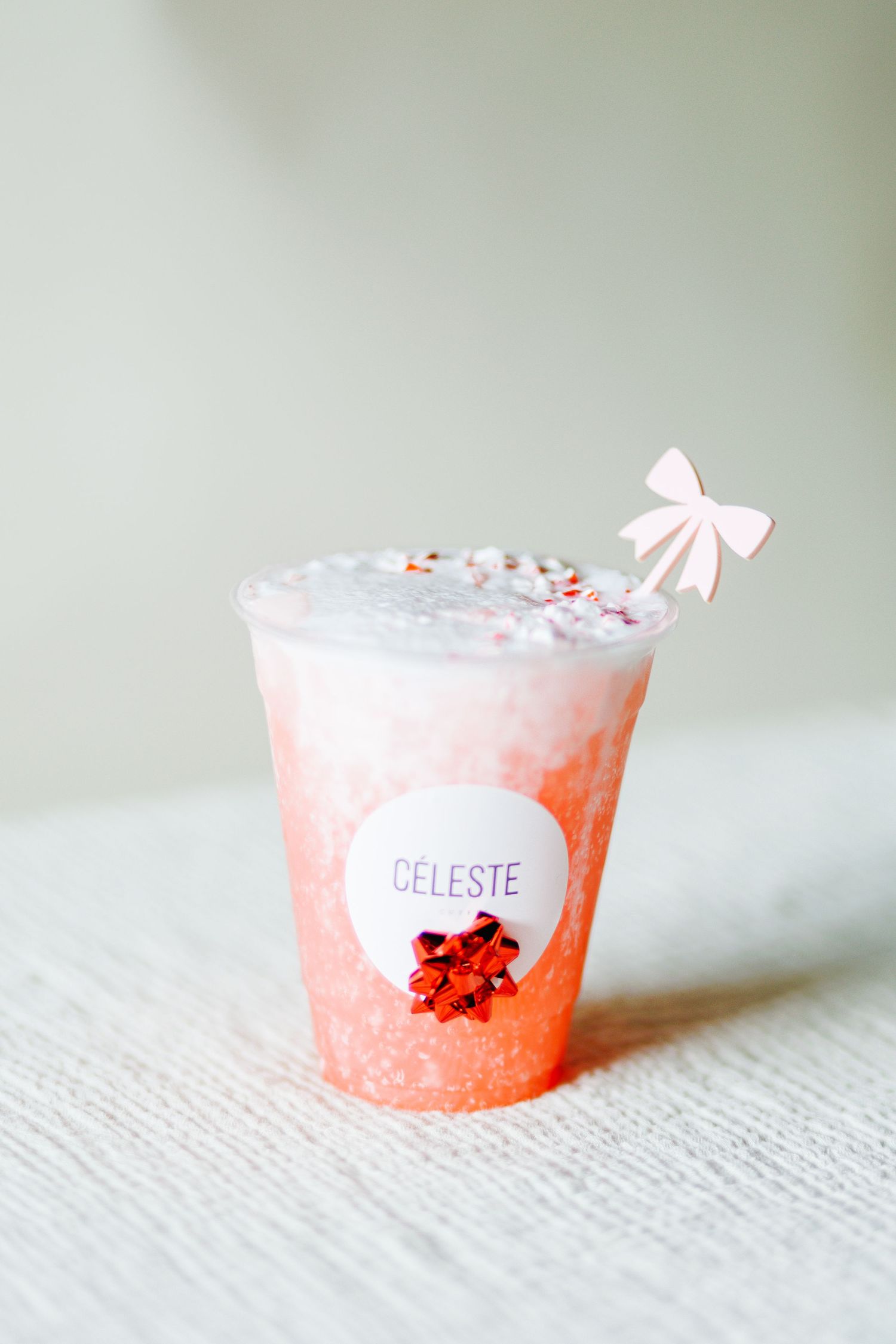 Pink holiday cocktail in a small cup decorated with a bow and sprinkles.