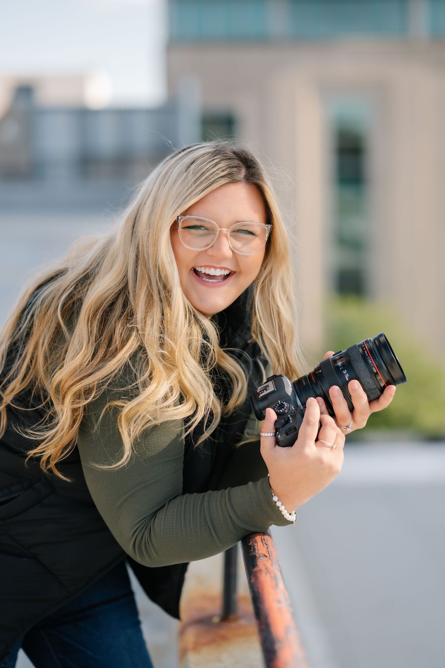 Photographer holds camera while posing playfully in outdoor photoshoot.