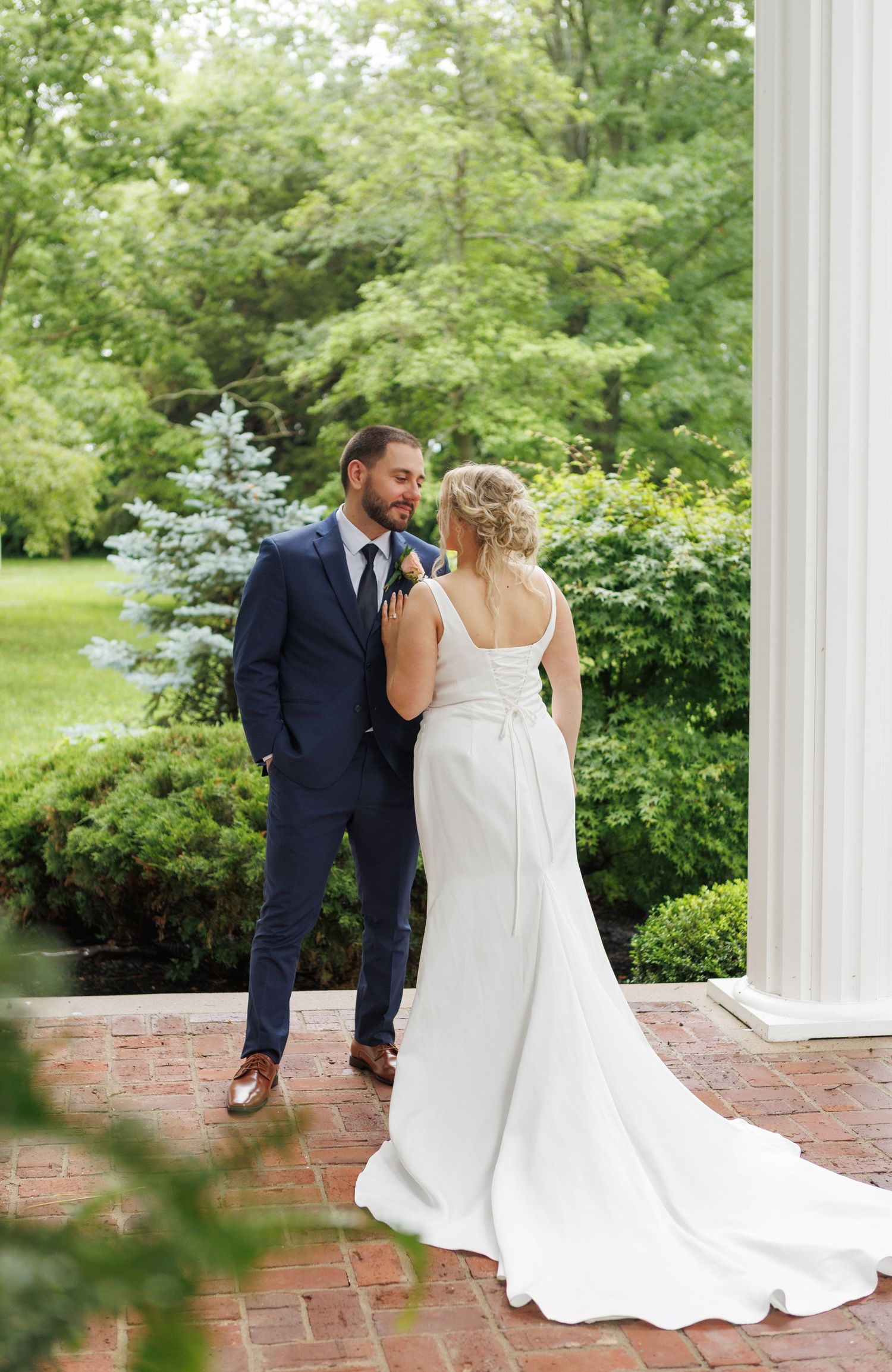 Bride and groom share a romantic moment on a brick patio surrounded by lush greenery at an elegant outdoor wedding.