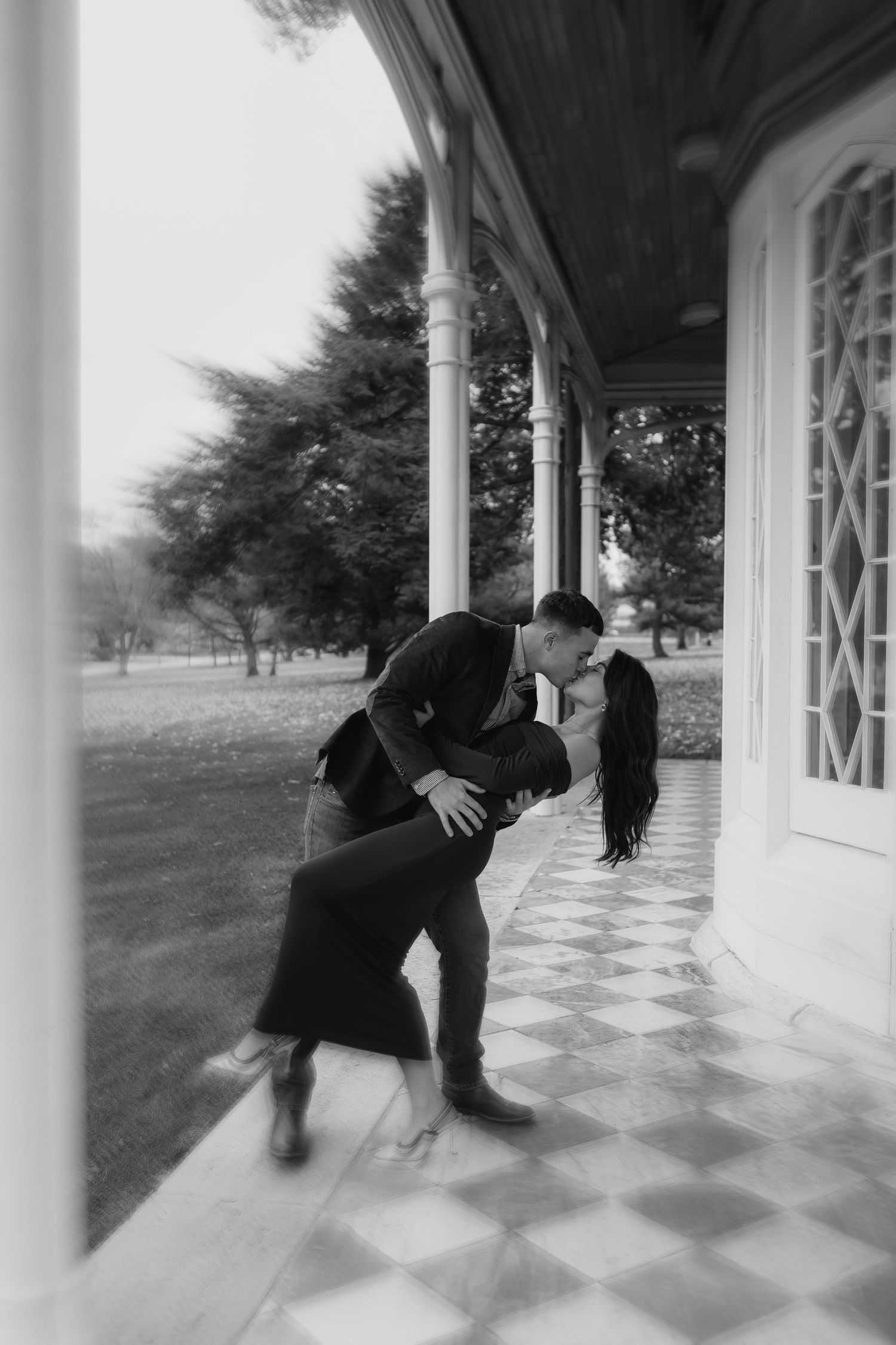 Romantic black and white photo of couple dancing on a vintage porch with classic architecture.