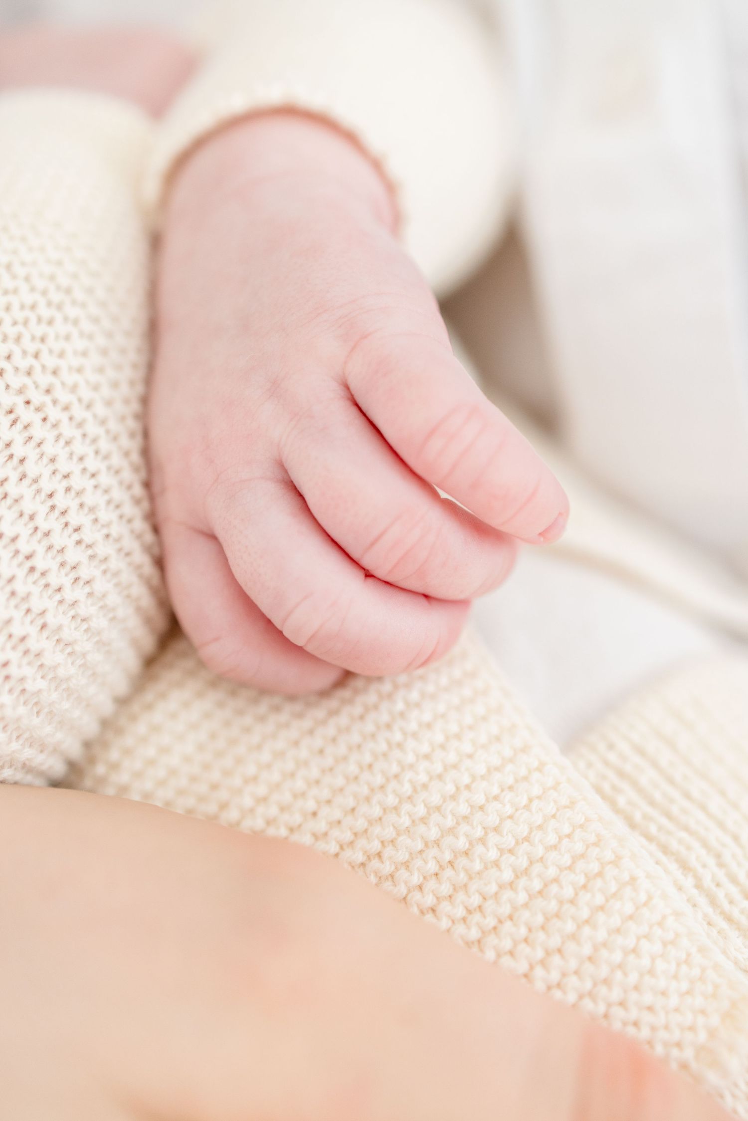 Close-up view of tiny baby hands touching soft cream-colored knitted fabric texture.