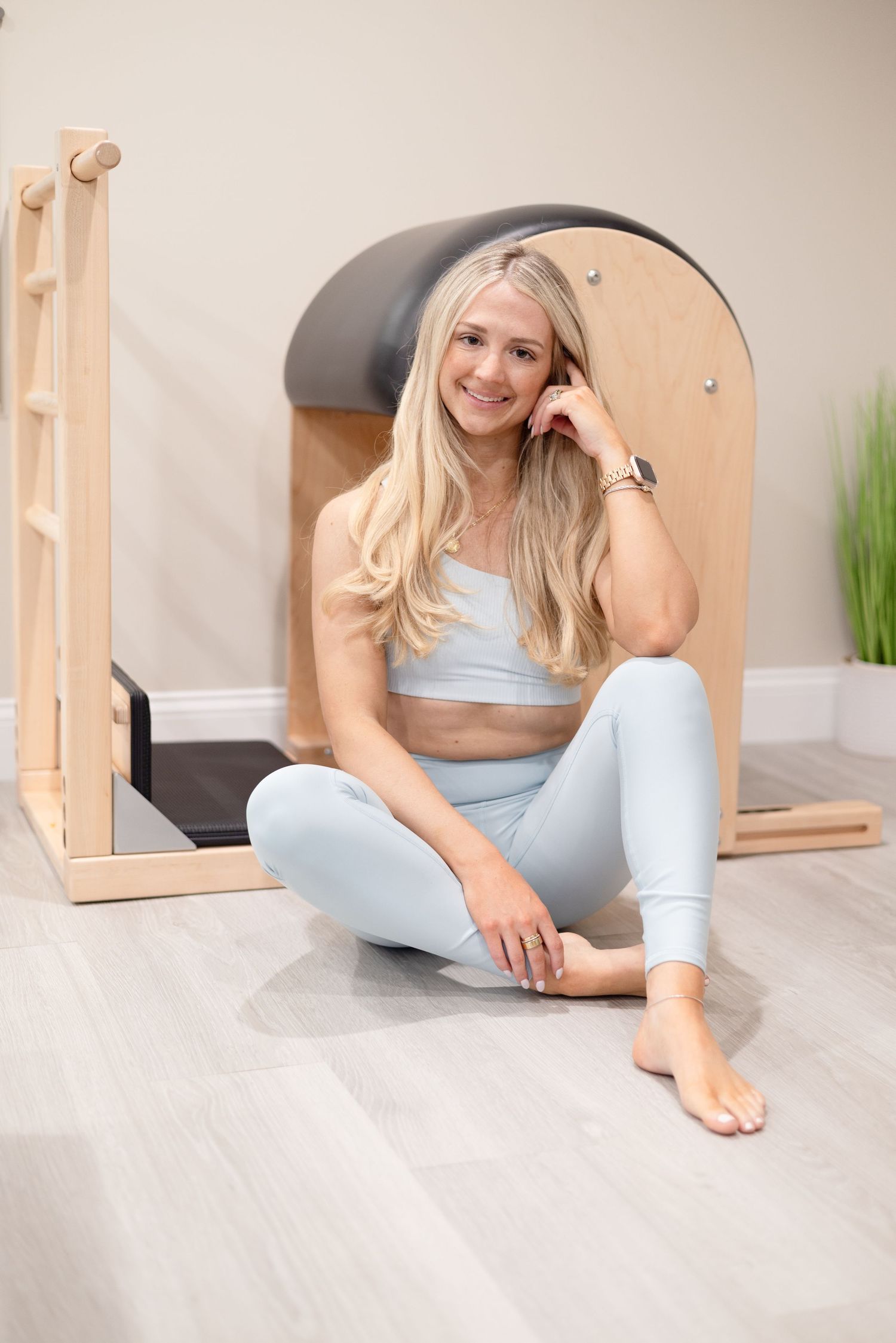 Person in workout attire sitting cross-legged on exercise equipment in a bright studio space.