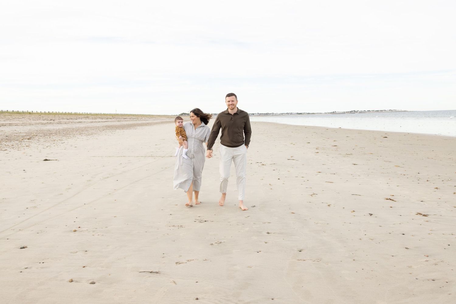 A couple strolls hand in hand along a serene beach with waves crashing in the distance.