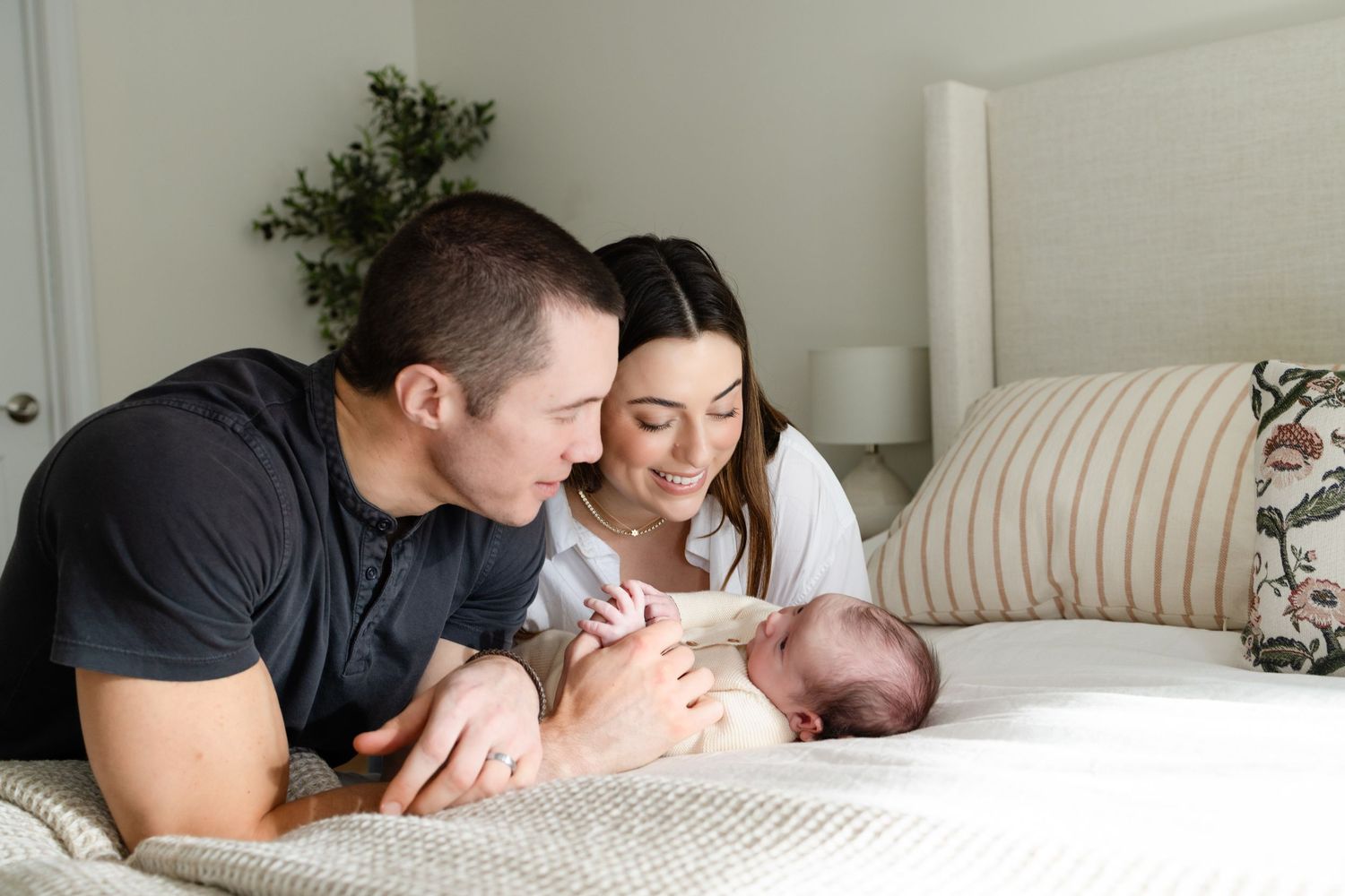 A parent and baby share tender moments while lying on a white bed.
