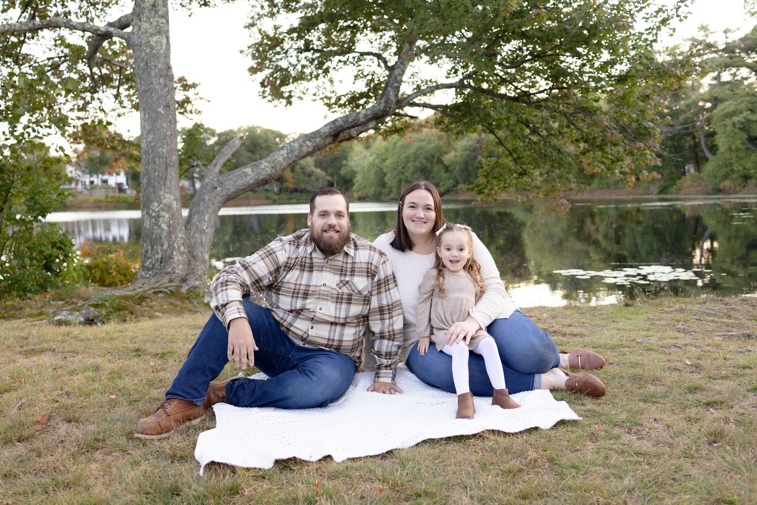 Family relaxing on blanket under trees during autumn outdoor session.