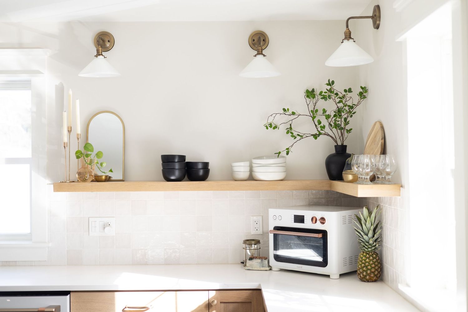 Minimalist kitchen with floating wooden shelf, white walls, and brass sconces.