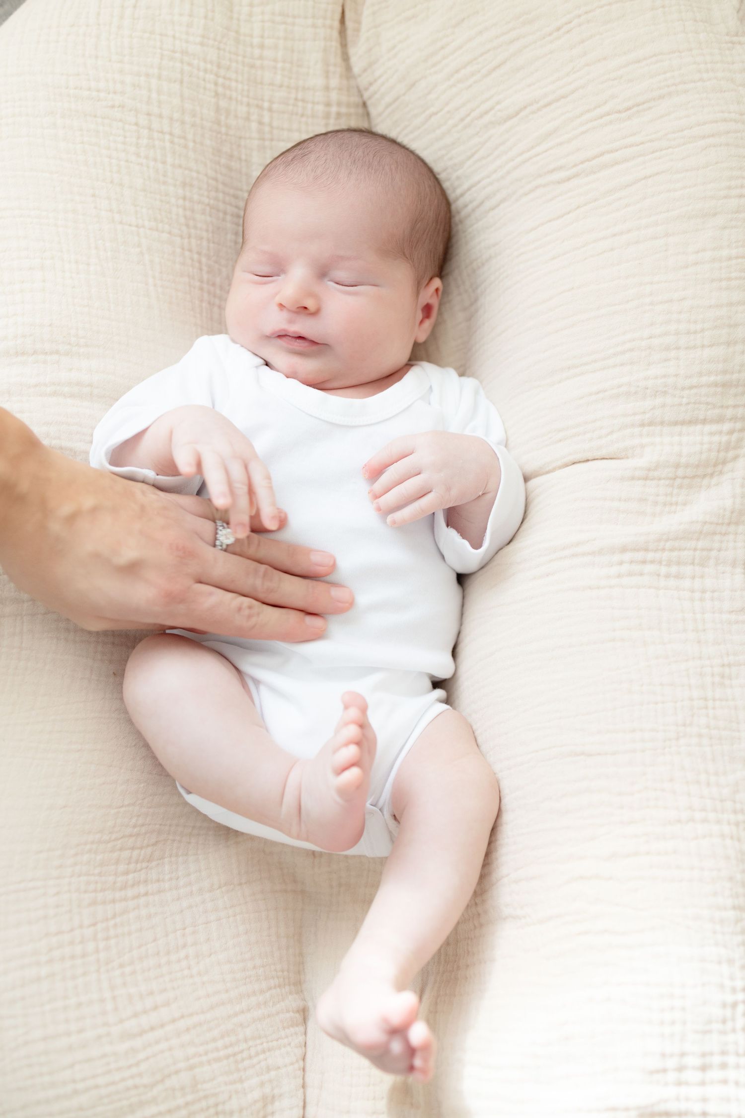 Sleeping infant in white onesie on cream colored bedding.