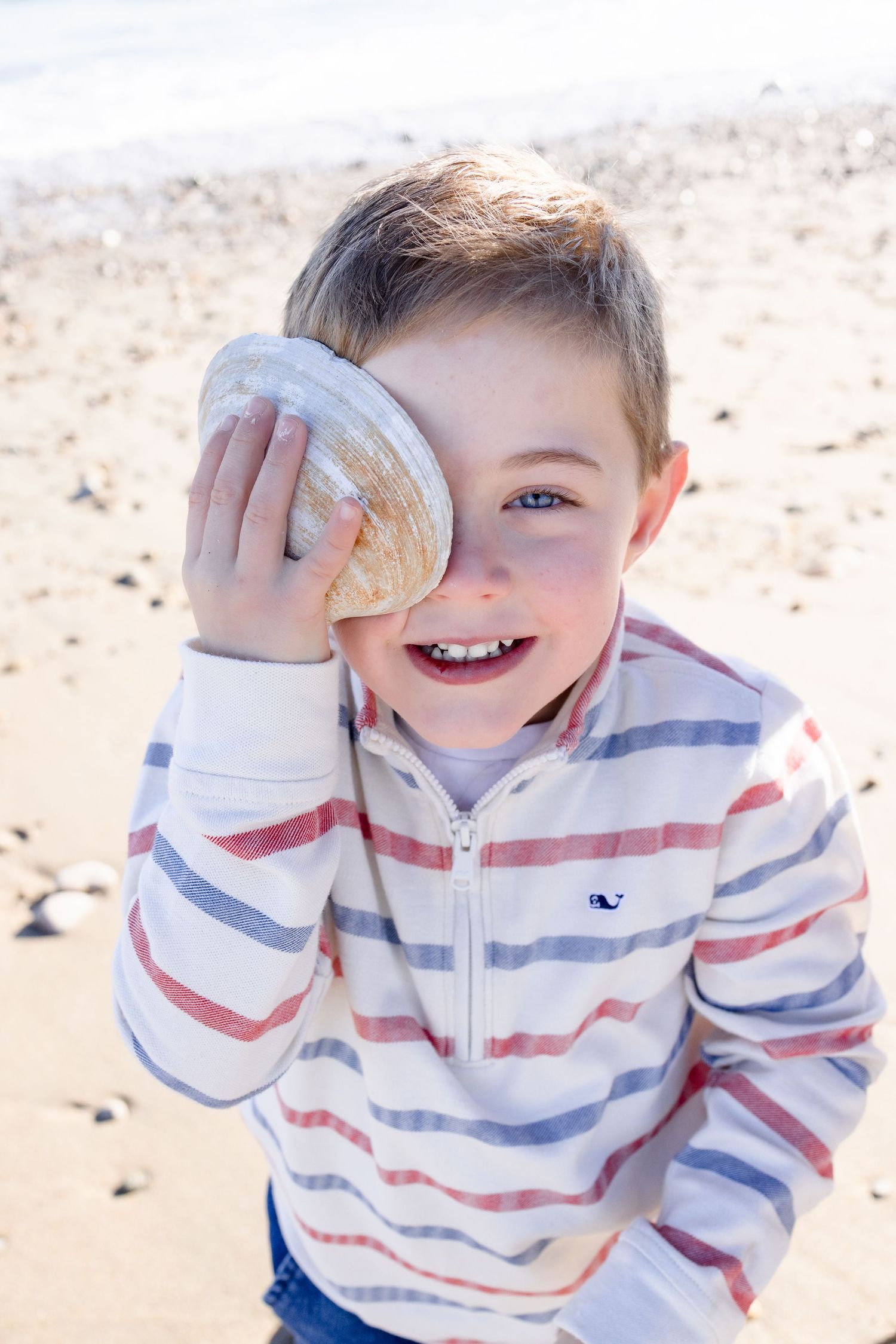 Child in striped sweater playing with seashells on beach.