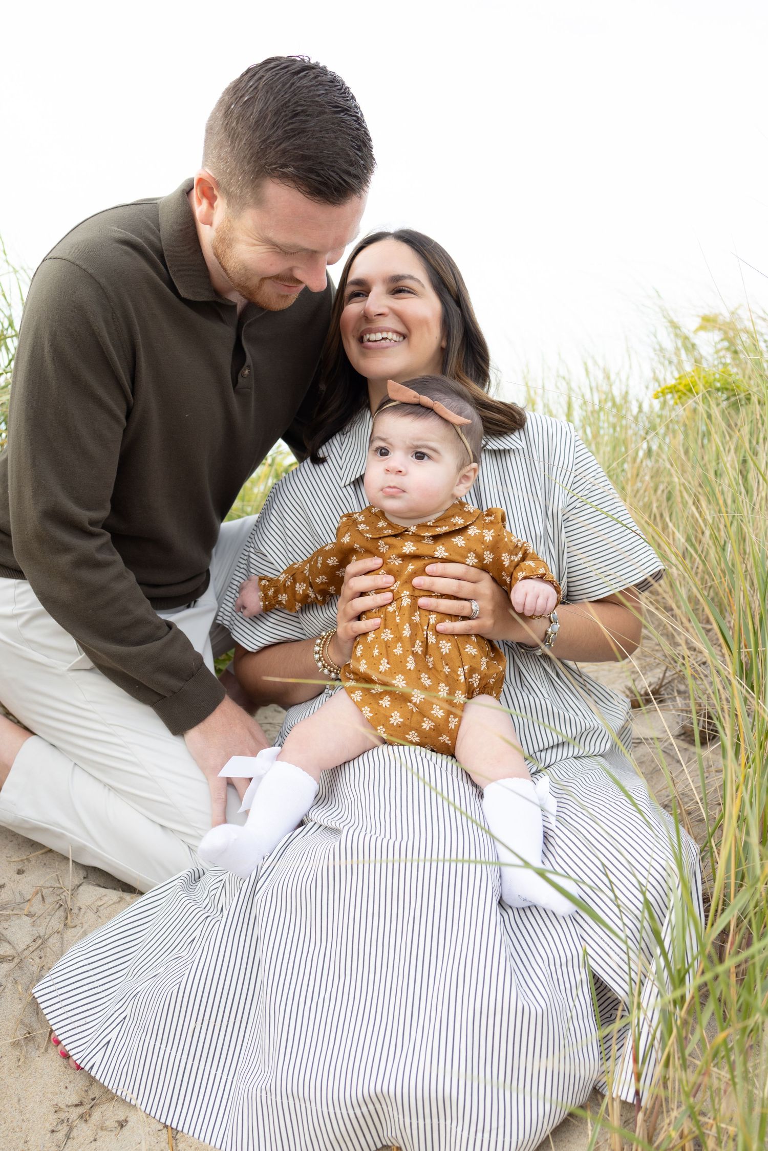 Candid family moments captured at sunset on a beach with tall grass in the background.