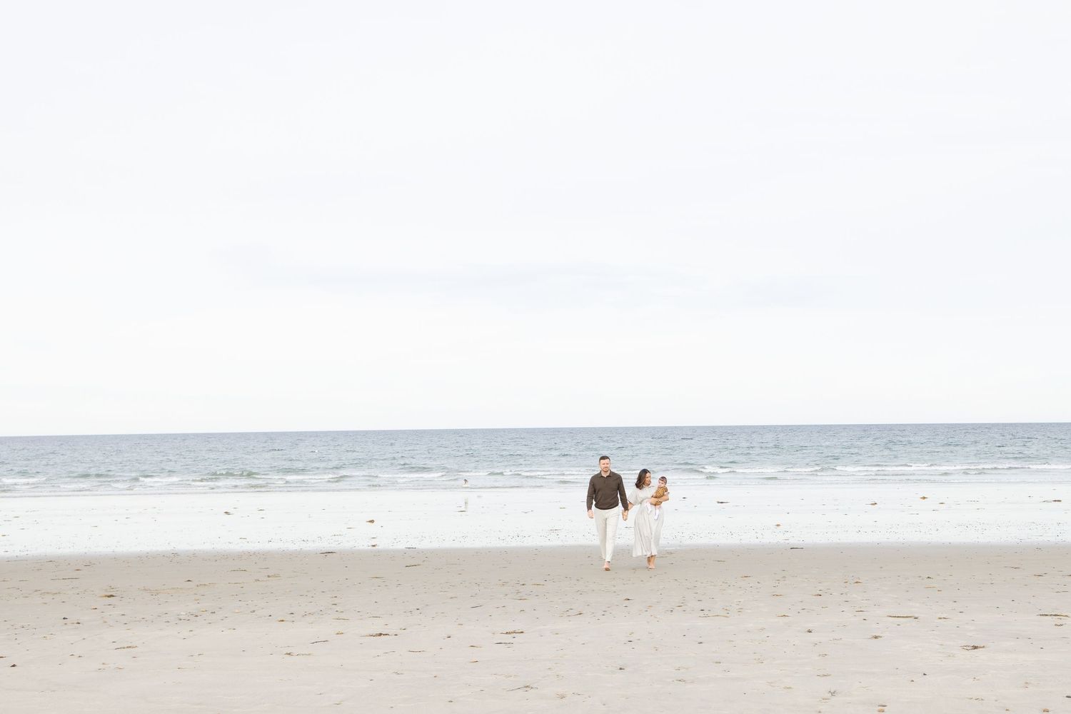 Two figures walk along an empty beach with soft white sky in the background.