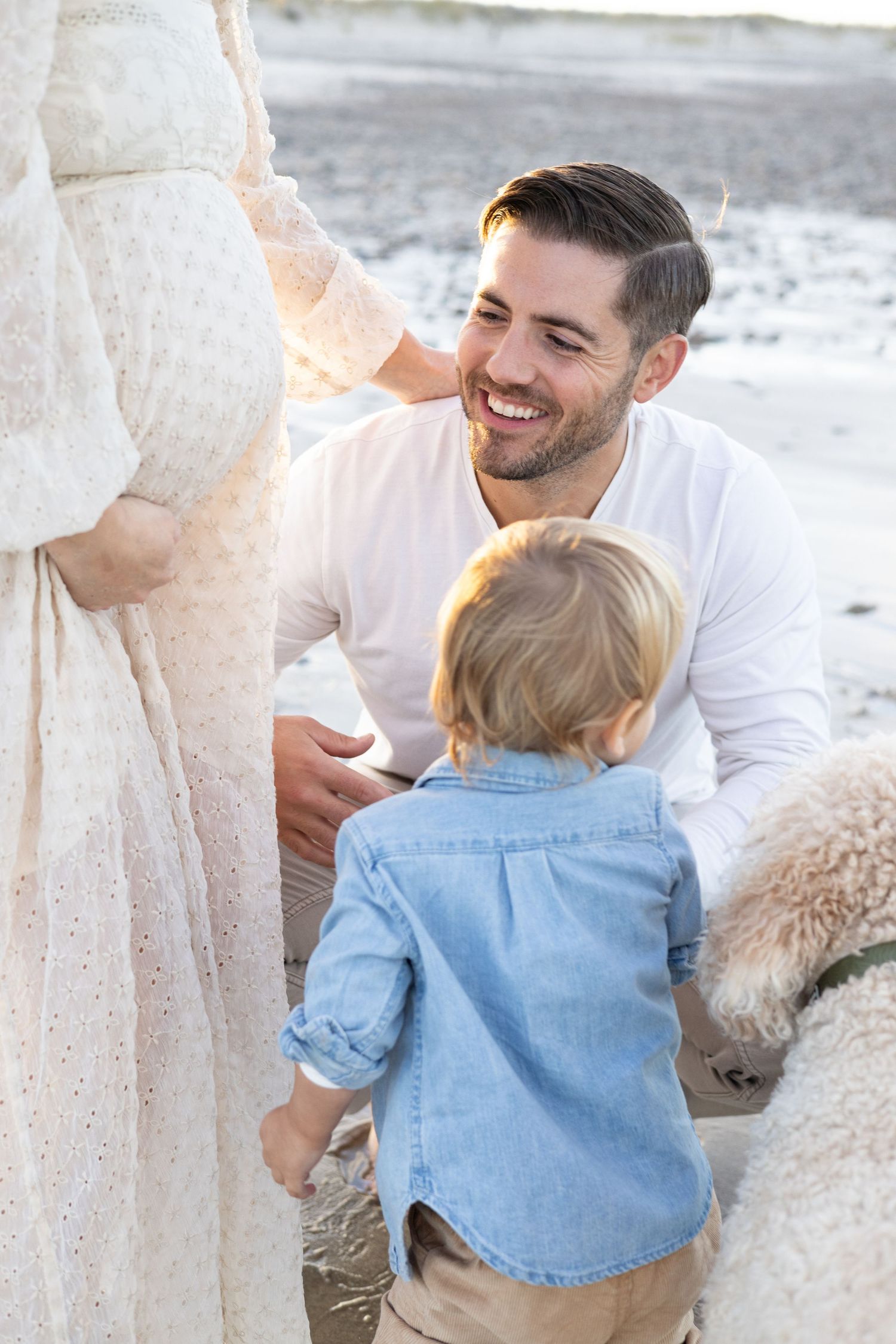 Family beach photoshoot with toddler in denim outfit against sandy backdrop.