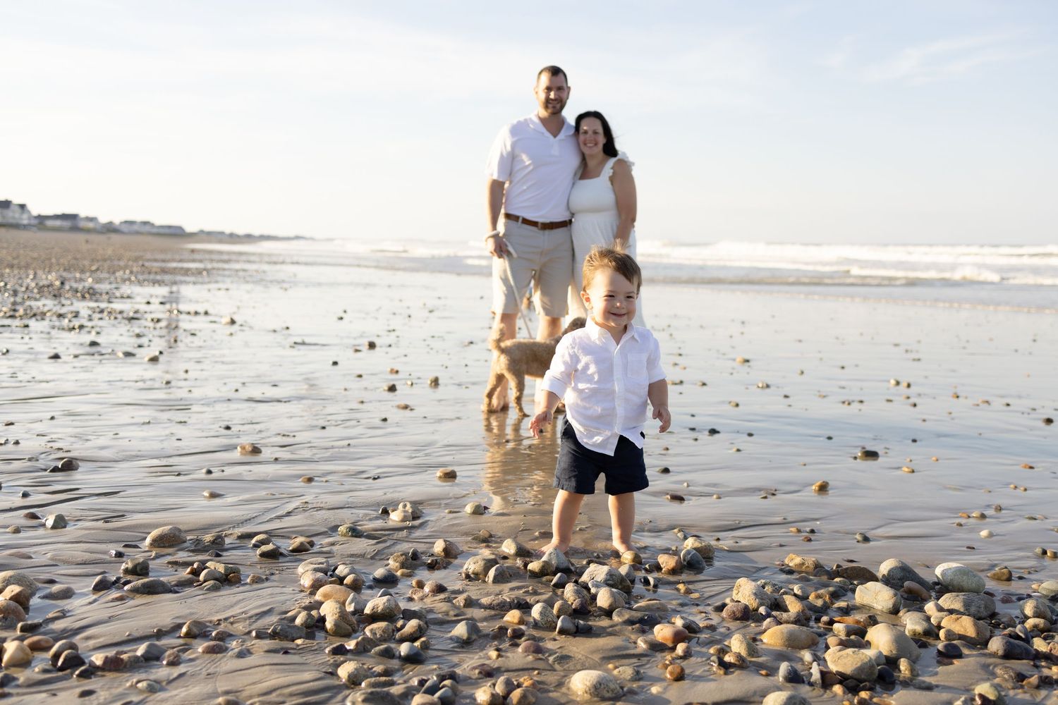 A family and their dog explore a rocky beach shoreline during sunset.