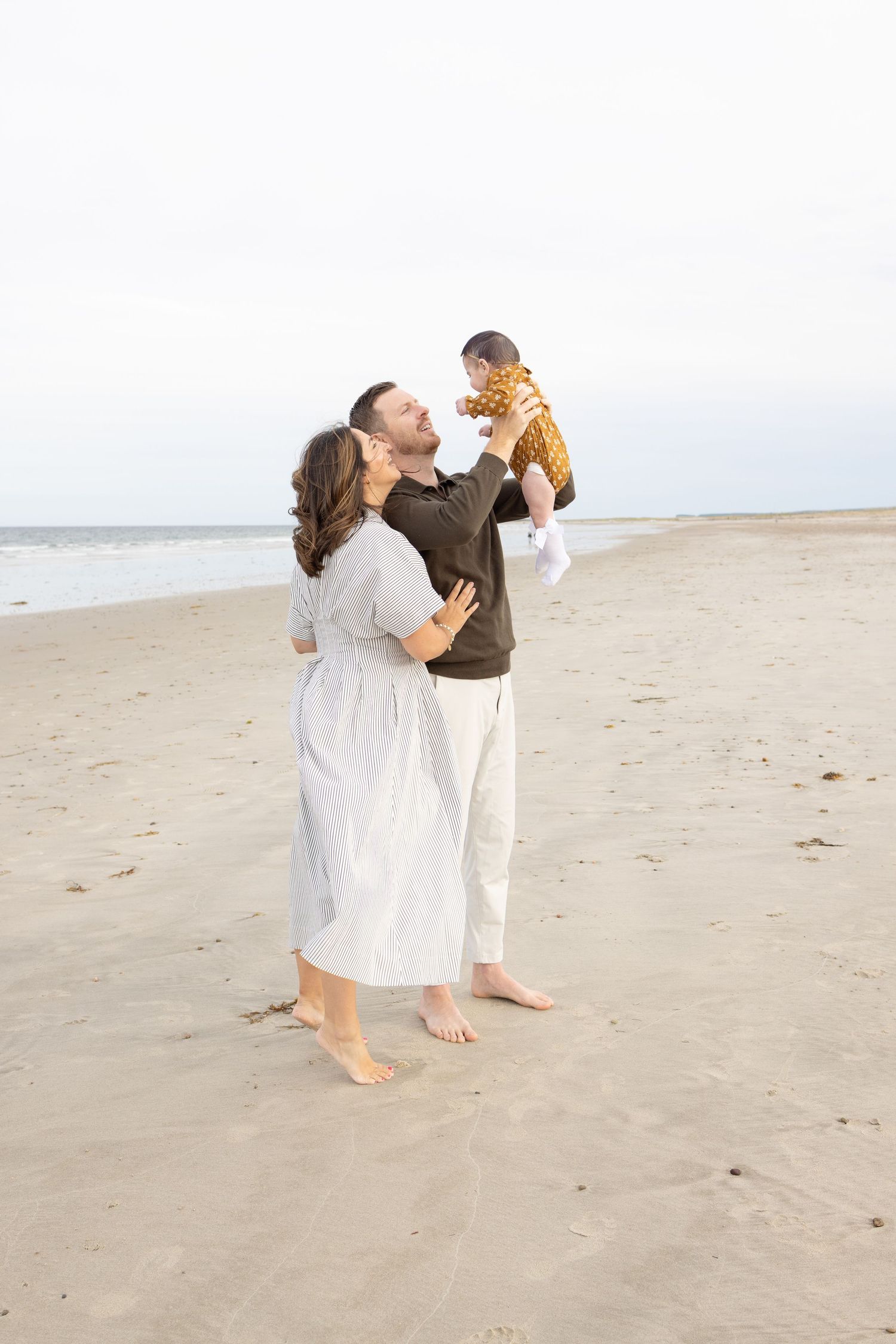 A couple shares a romantic moment while walking on a sandy beach in white attire.