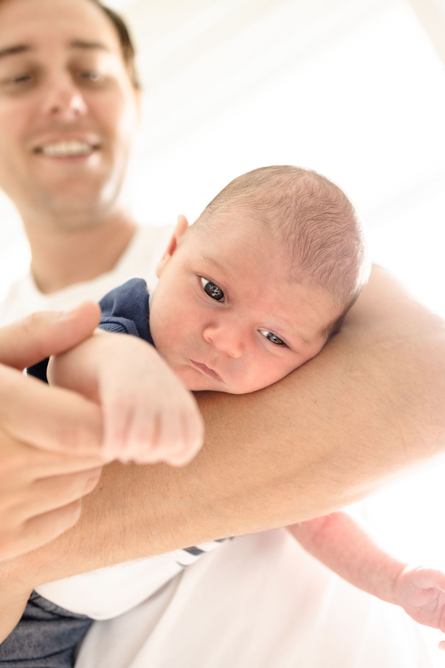 A smiling father cradling his newborn baby on his forearm, with the infant looking alert and curious.