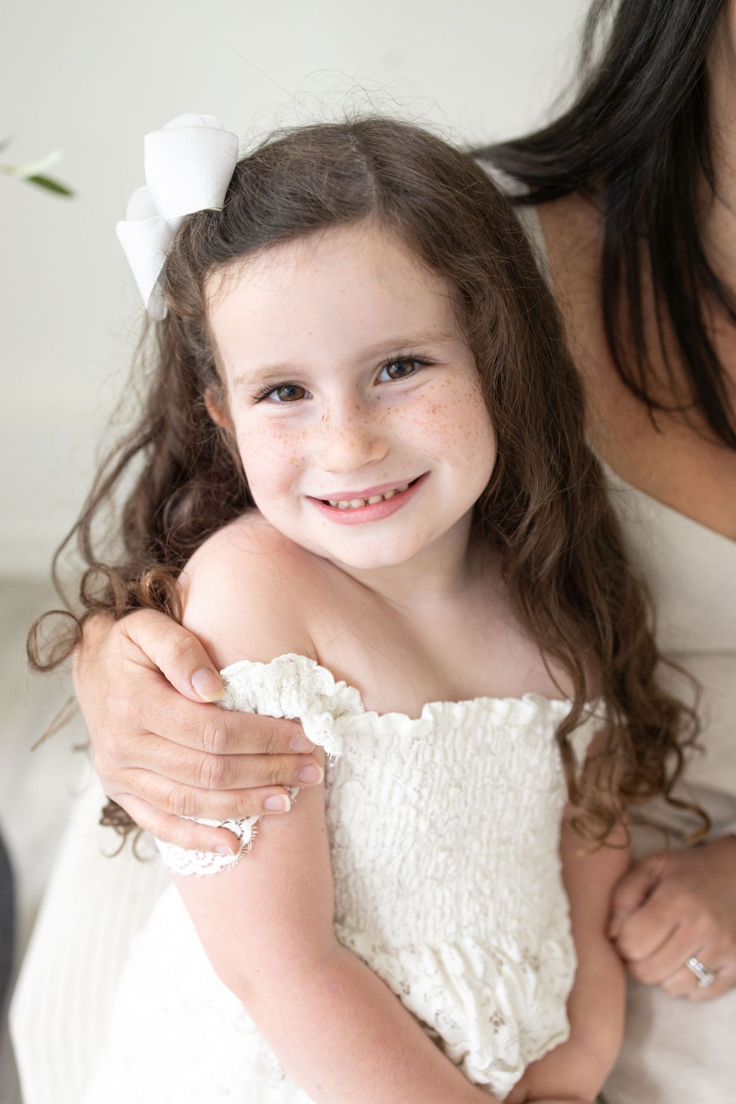 Young child wearing white smocked dress in bright studio setting.