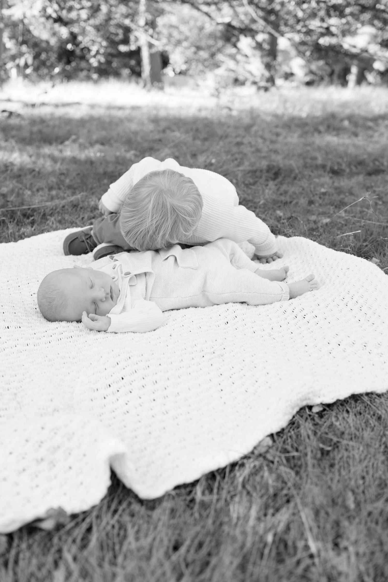 Baby resting on white knit blanket in black and white outdoor photo.