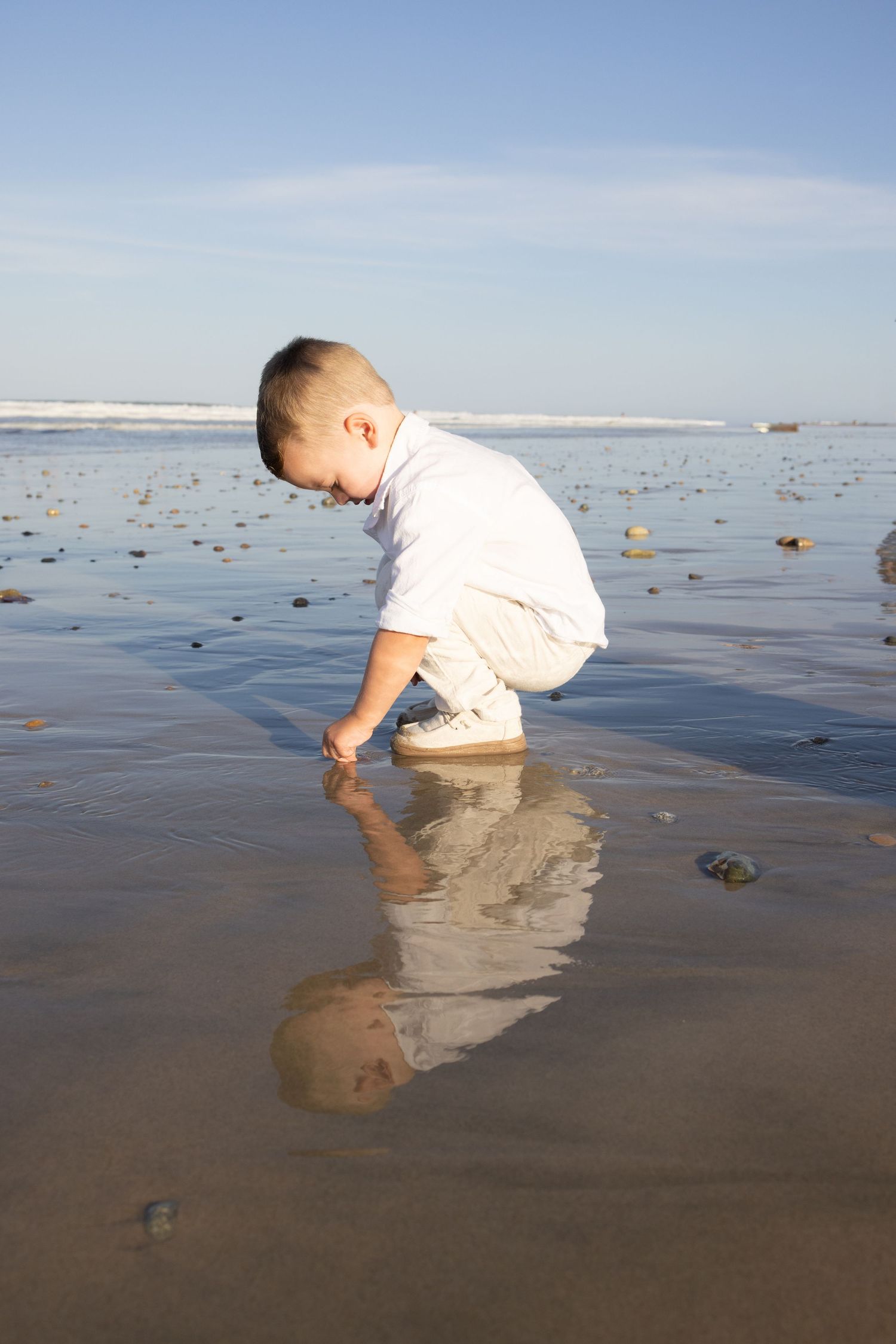 Child playing in wet sand at beach with reflection in water.