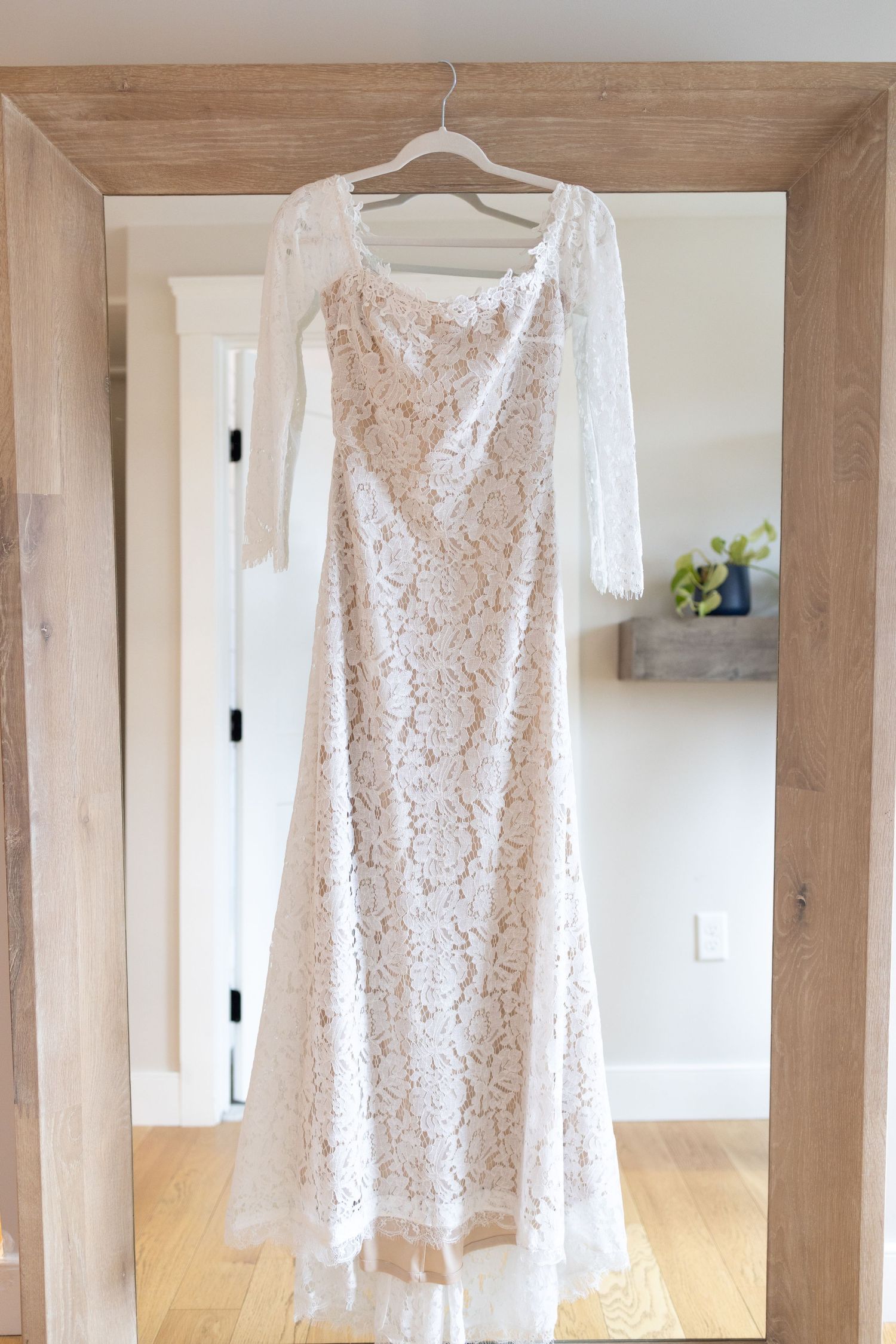 White lace wedding dress hanging in modern wooden interior.