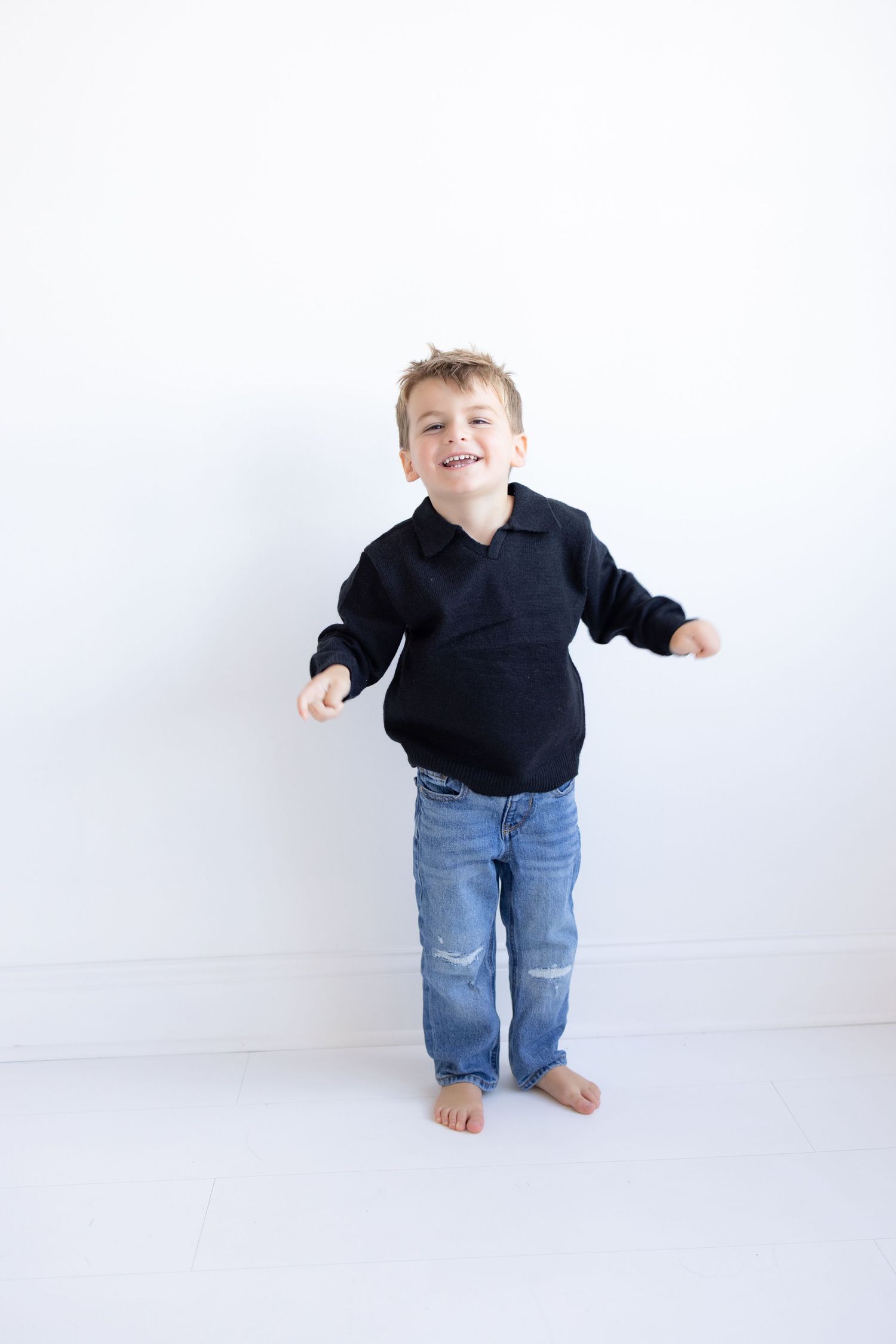Small child in black sweater and jeans playing against white background.