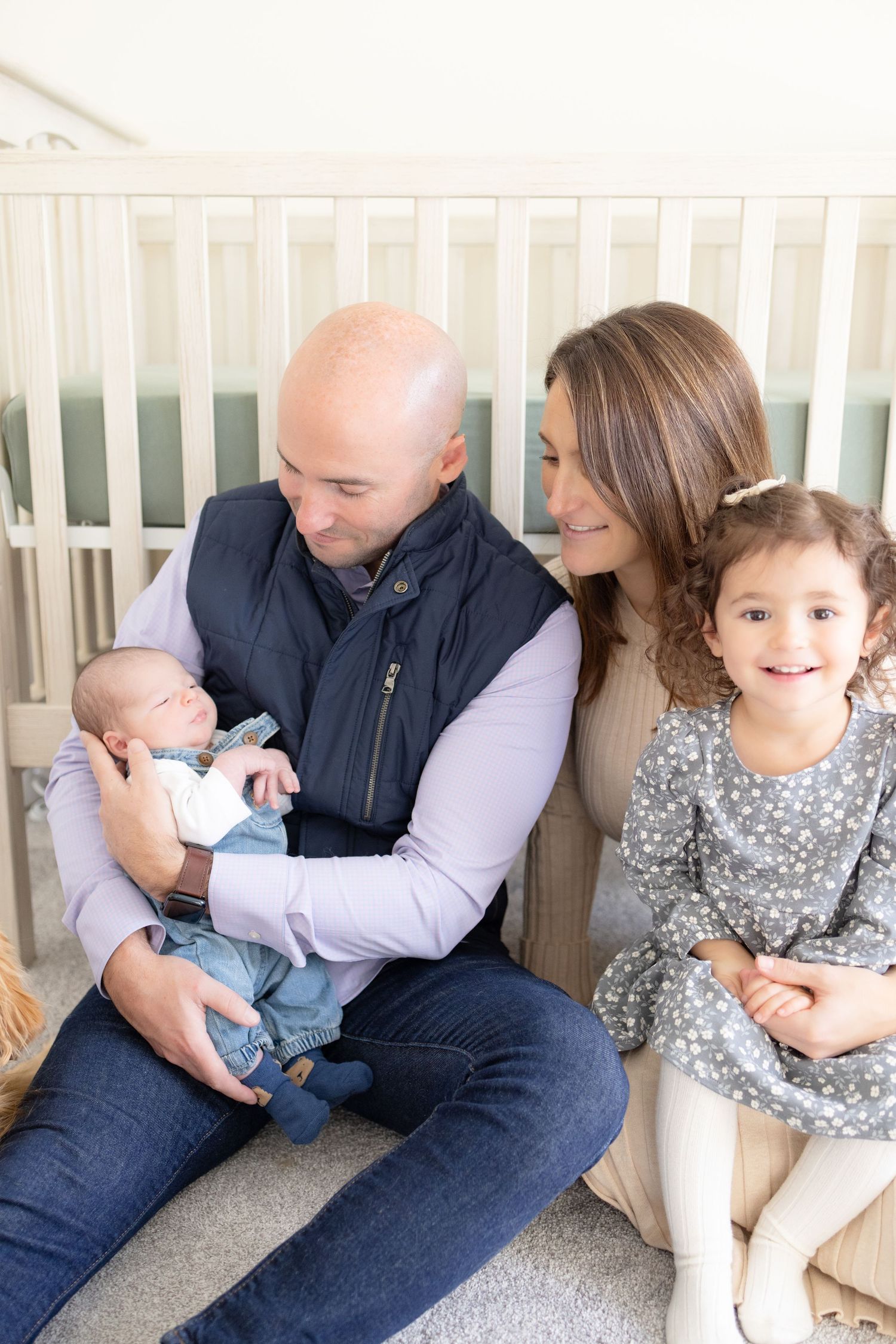 Family sitting together on white porch bench with newborn and toddler.