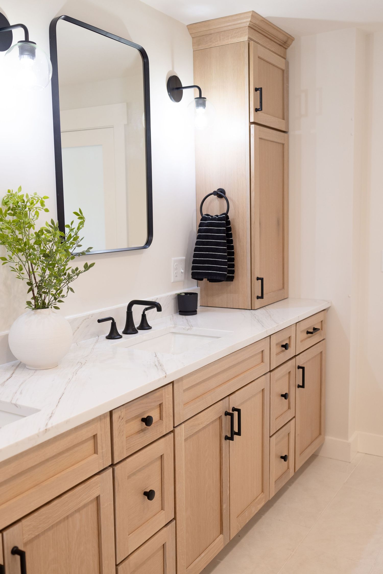 Light wood bathroom vanity with black hardware, marble countertop, and modern black-framed mirror.