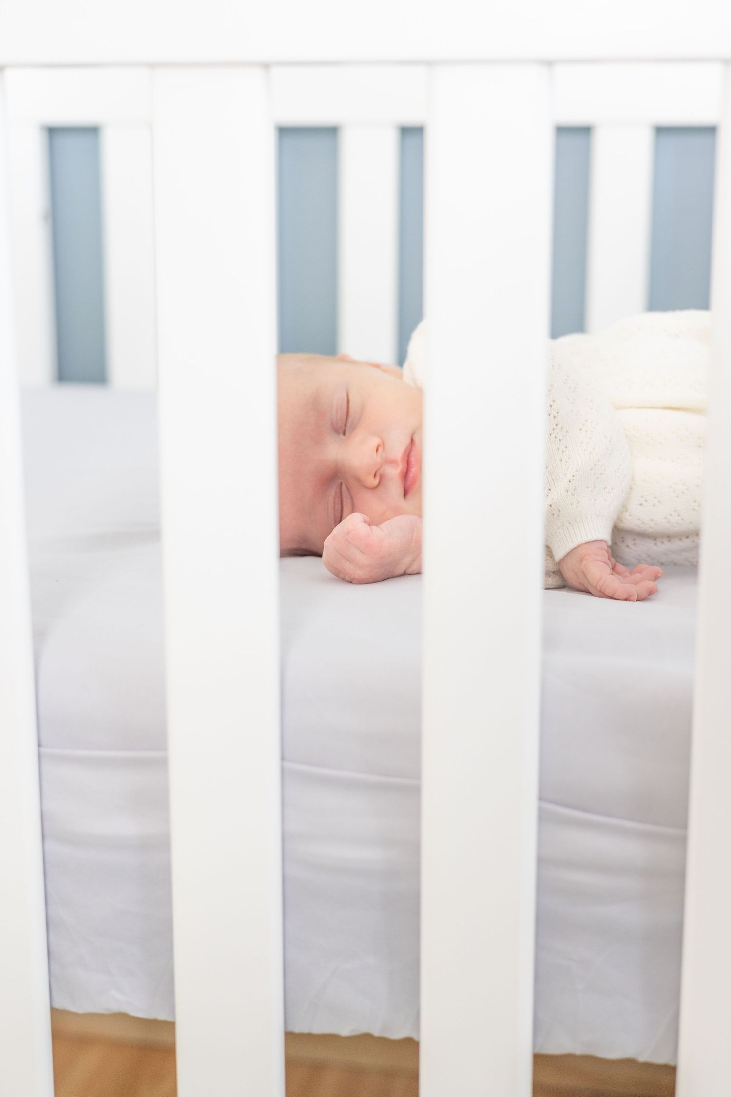 Close-up view of white crib slats with mattress inside.