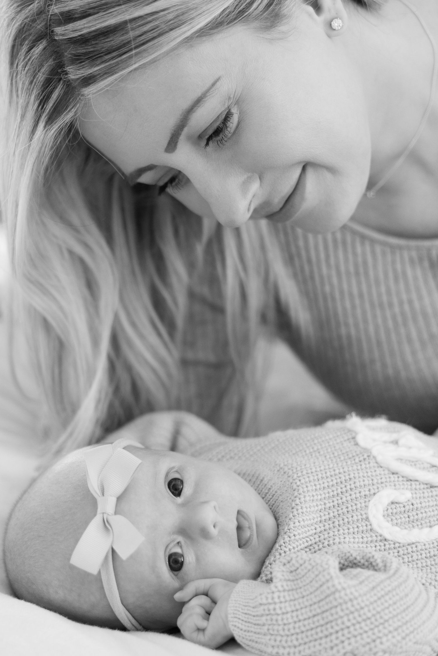 Woman in gray sweater tenderly bonding with baby in white knit outfit.