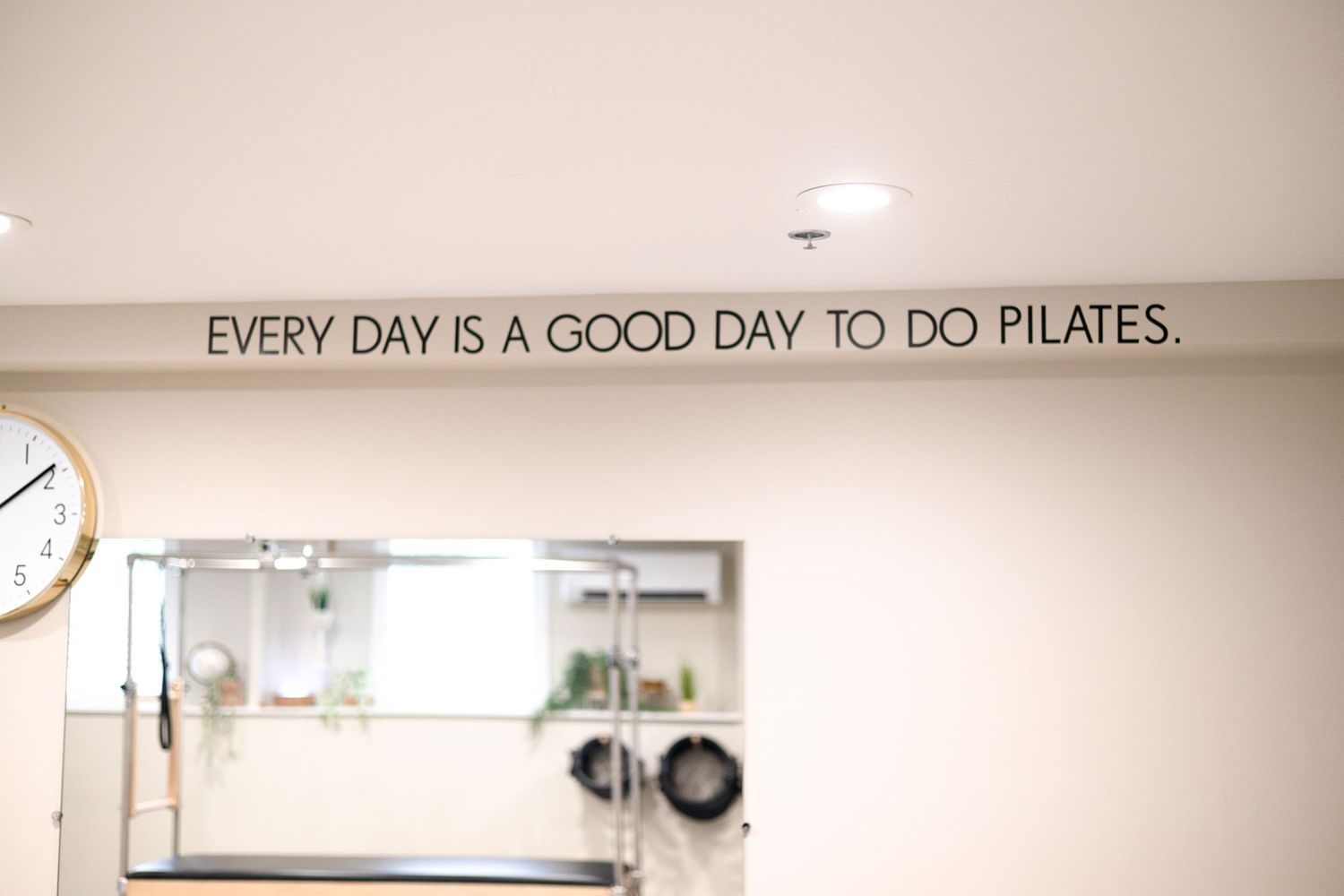 Text on wall reading 'Every day is a good day to do pilates' in a bright studio space.