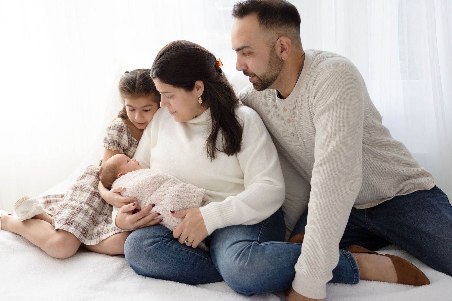 Parents and newborn share tender moments together on a white bed.
