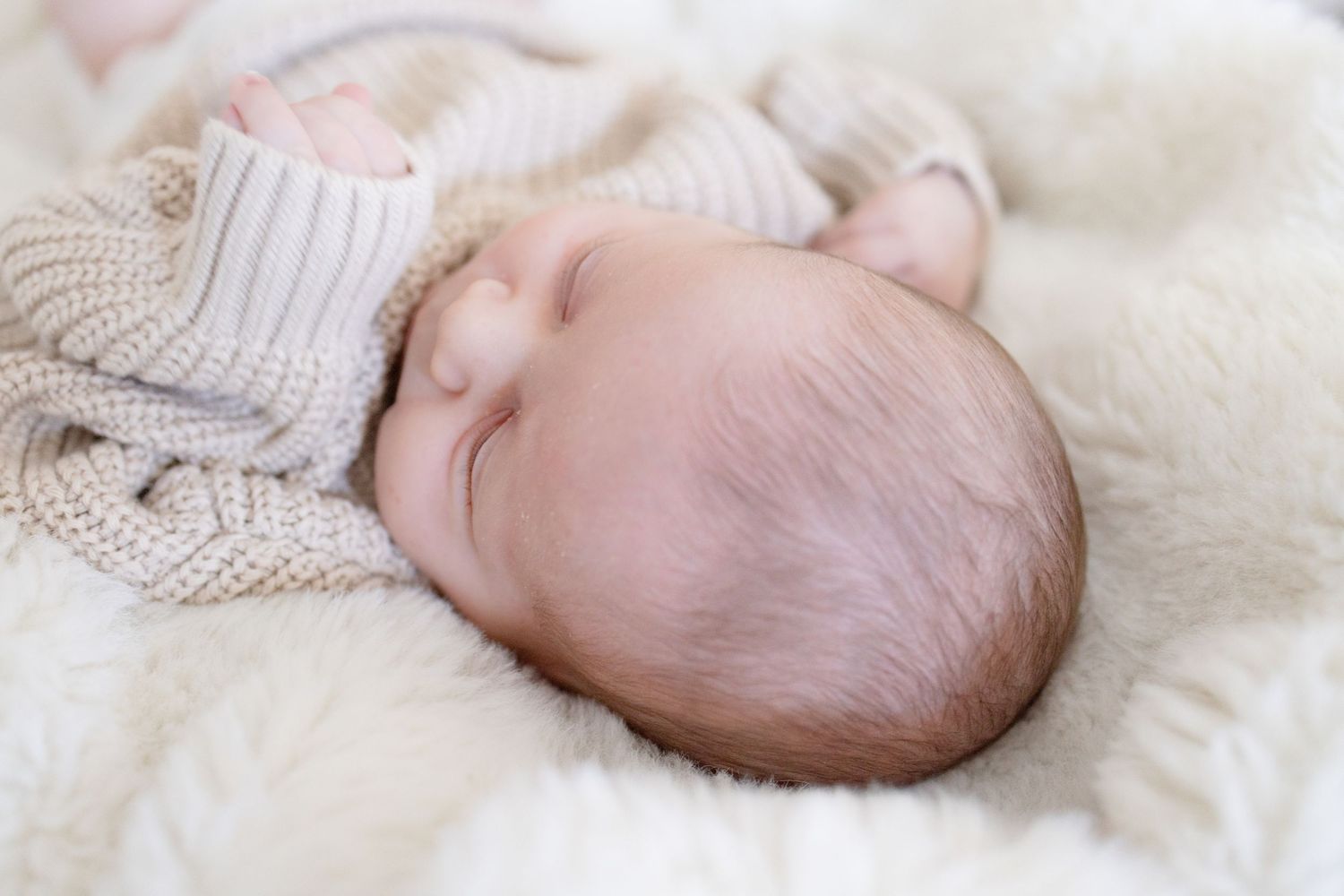 Sleeping infant wrapped in cozy knit blanket on soft white bedding.