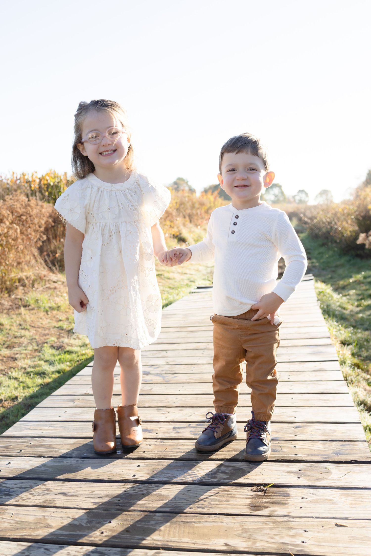 Two children standing on wooden boardwalk in sunlit outdoor setting.